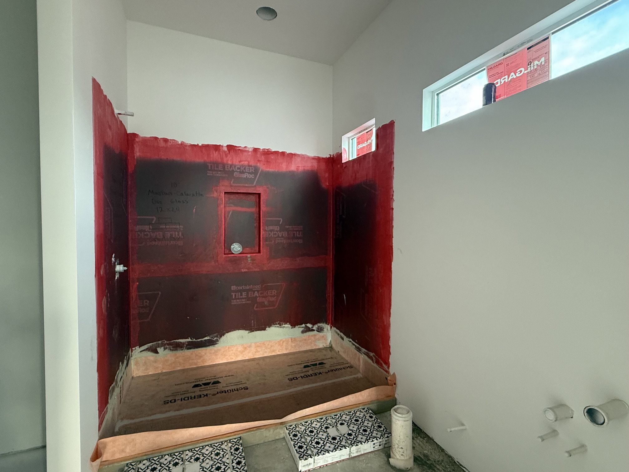 Shower enclosure featuring waterproof membrane installation, a recessed niche, uninstalled tile samples, and a high horizontal window