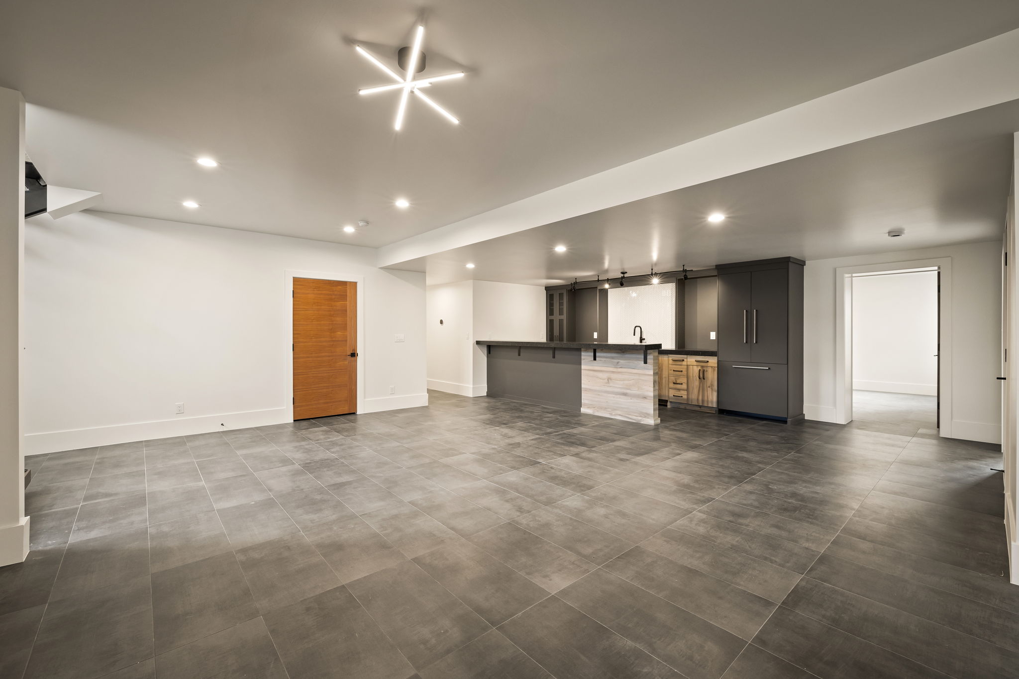 Open-concept recreation room featuring modern tile flooring, recessed lighting, and a contemporary linear chandelier