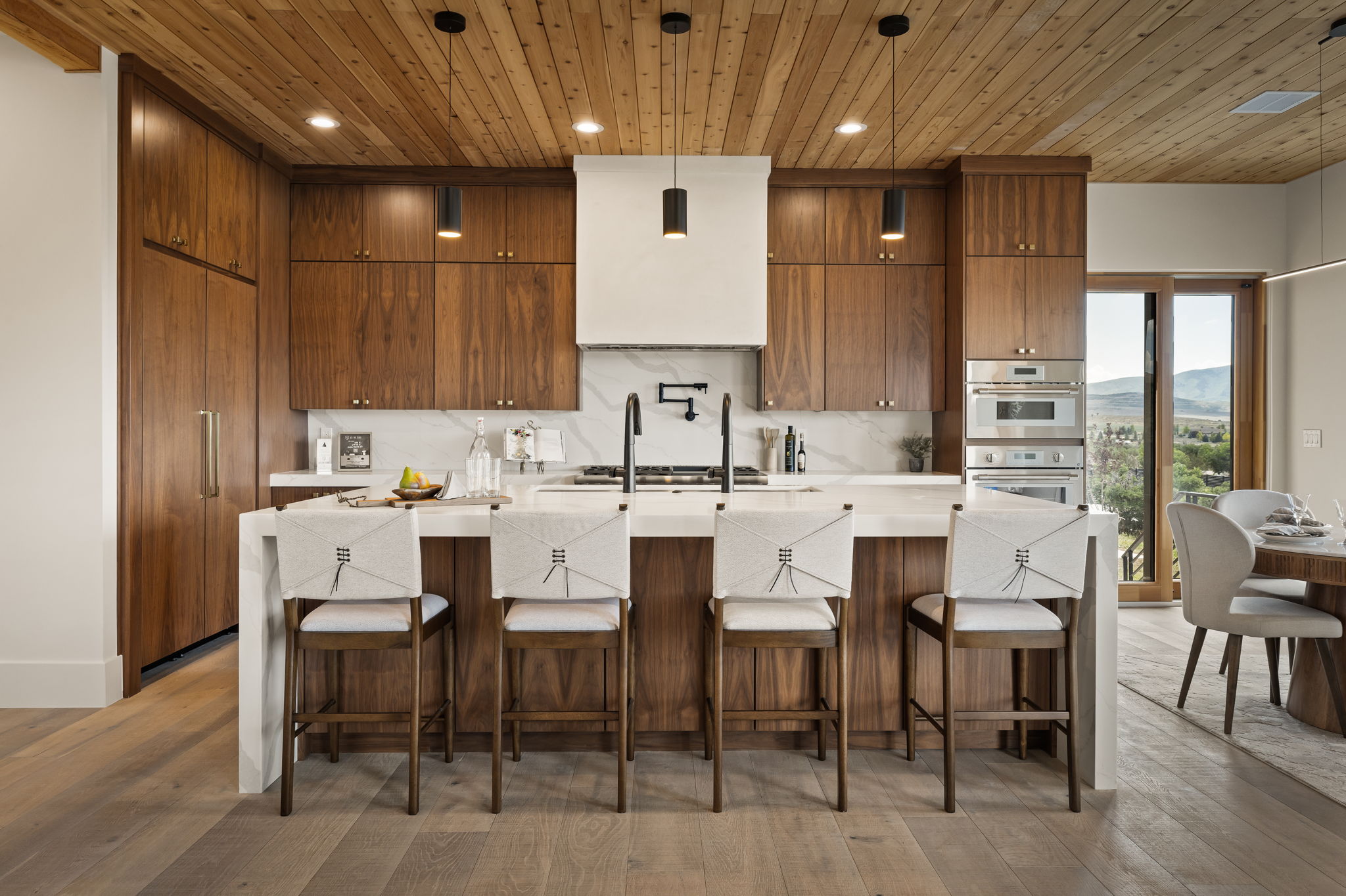 Kitchen featuring custom wood cabinetry, a large center island with seating, integrated appliances, built-in wall oven and microwave, and wood-paneled ceilings