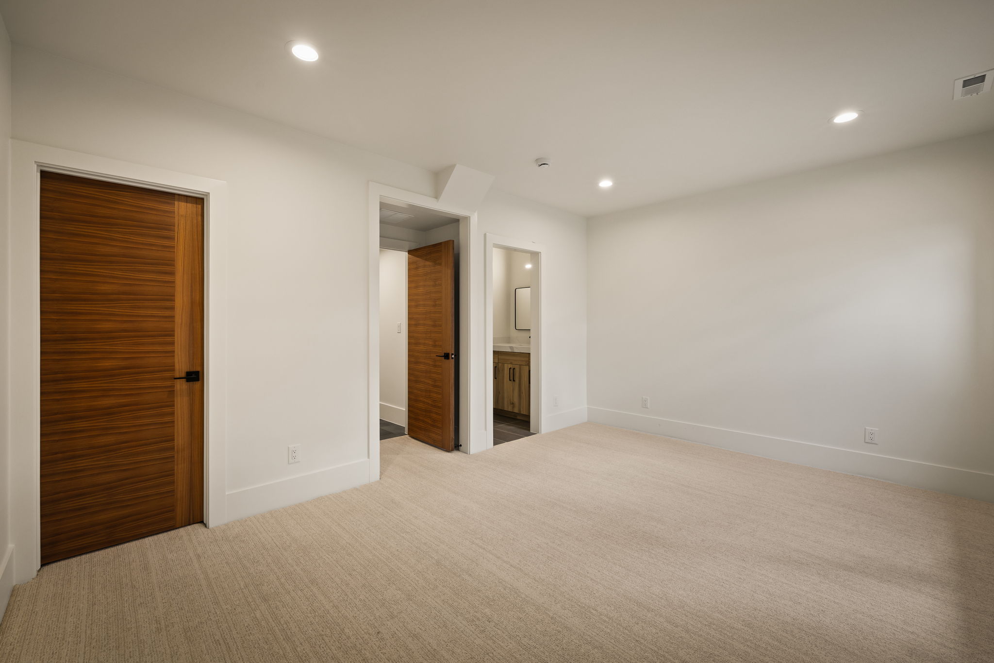 Spacious room featuring neutral carpet flooring, recessed lighting, and contemporary wood-grain doors with matte black hardware