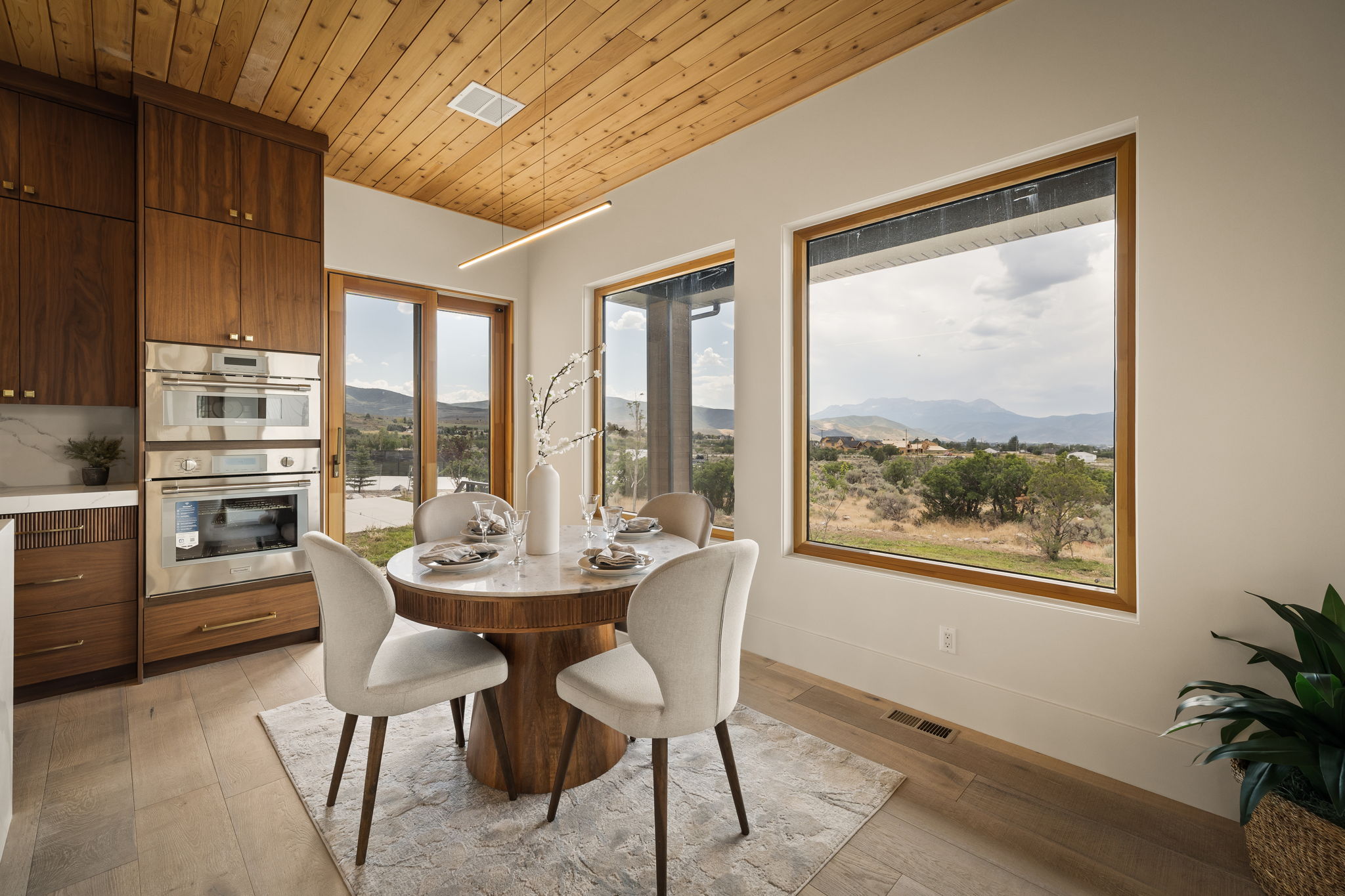 Dining area with large windows, a wood-plank ceiling, built-in stainless steel double ovens, and rich wood cabinetry