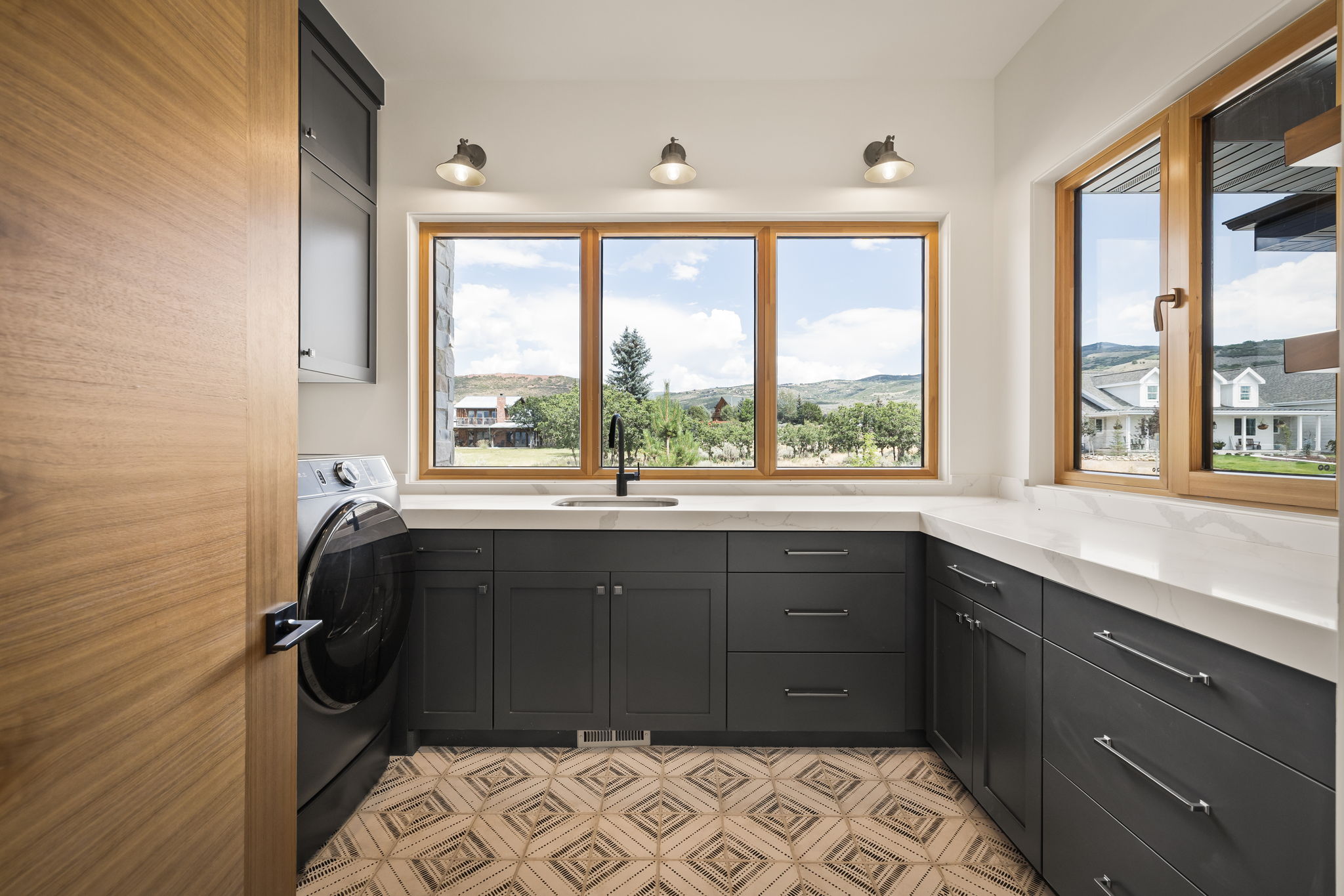 Laundry room featuring extensive counter space with a built-in sink, ample cabinetry, wood-finish window frames, and decorative tiled flooring