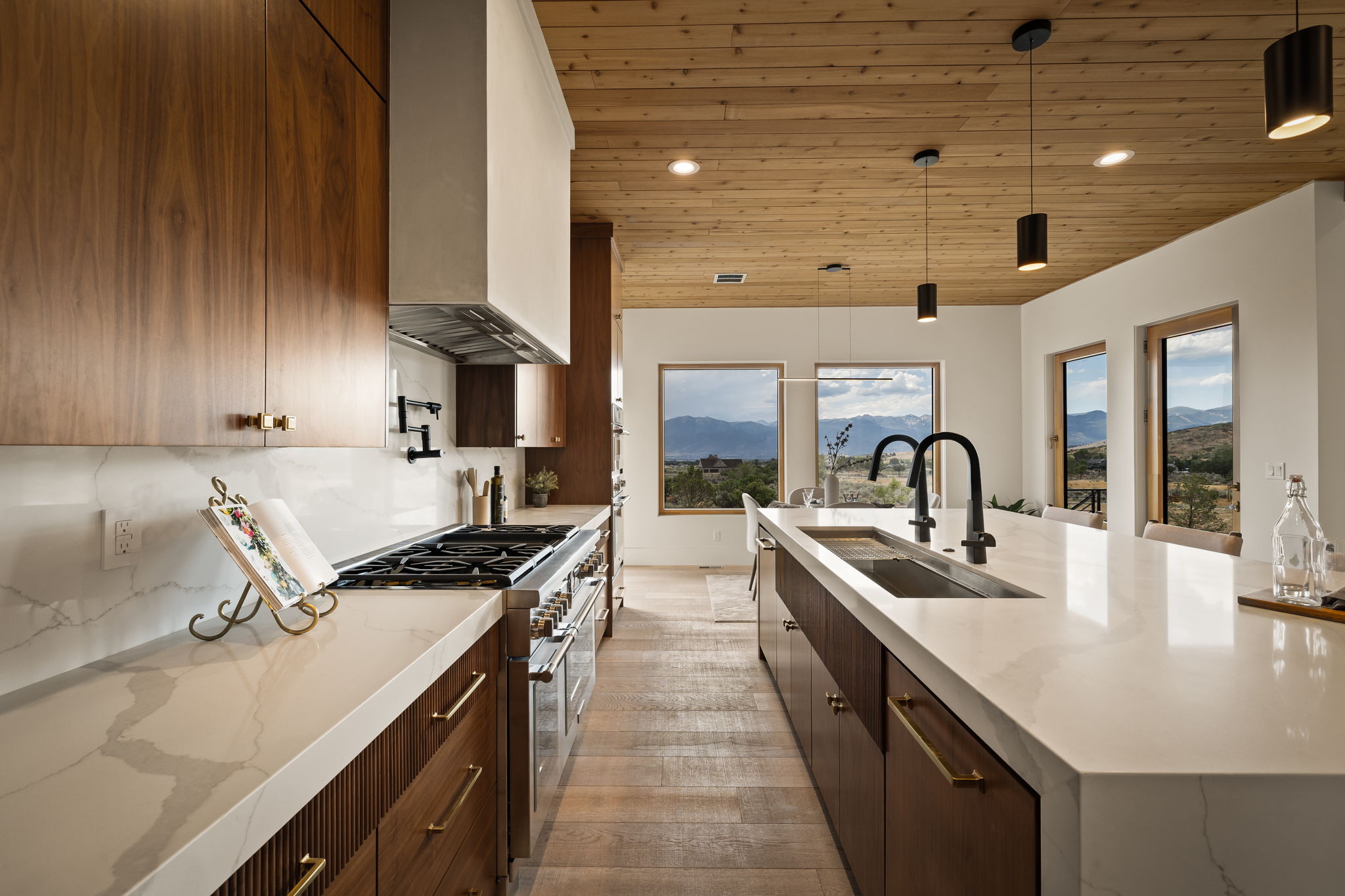 Modern kitchen featuring extensive wood-finish cabinetry, white countertops, a professional-grade range, and a large island with an integrated sink and dual faucets