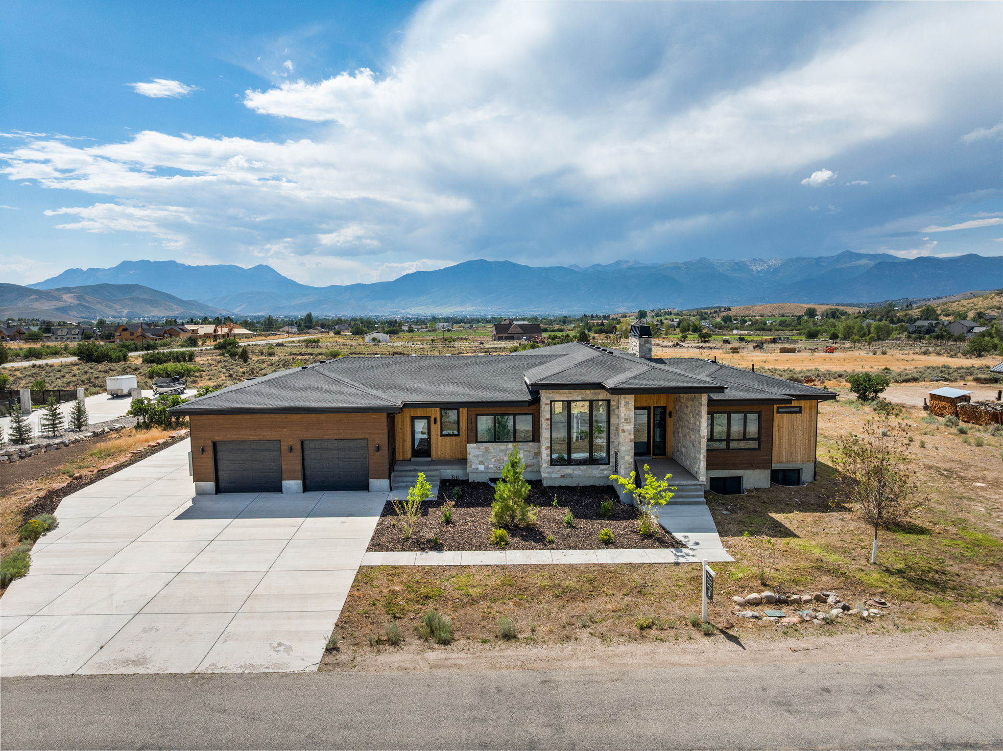Modern ranch-style residence featuring a prominent stone facade, wood paneling, and a dark shingle roof