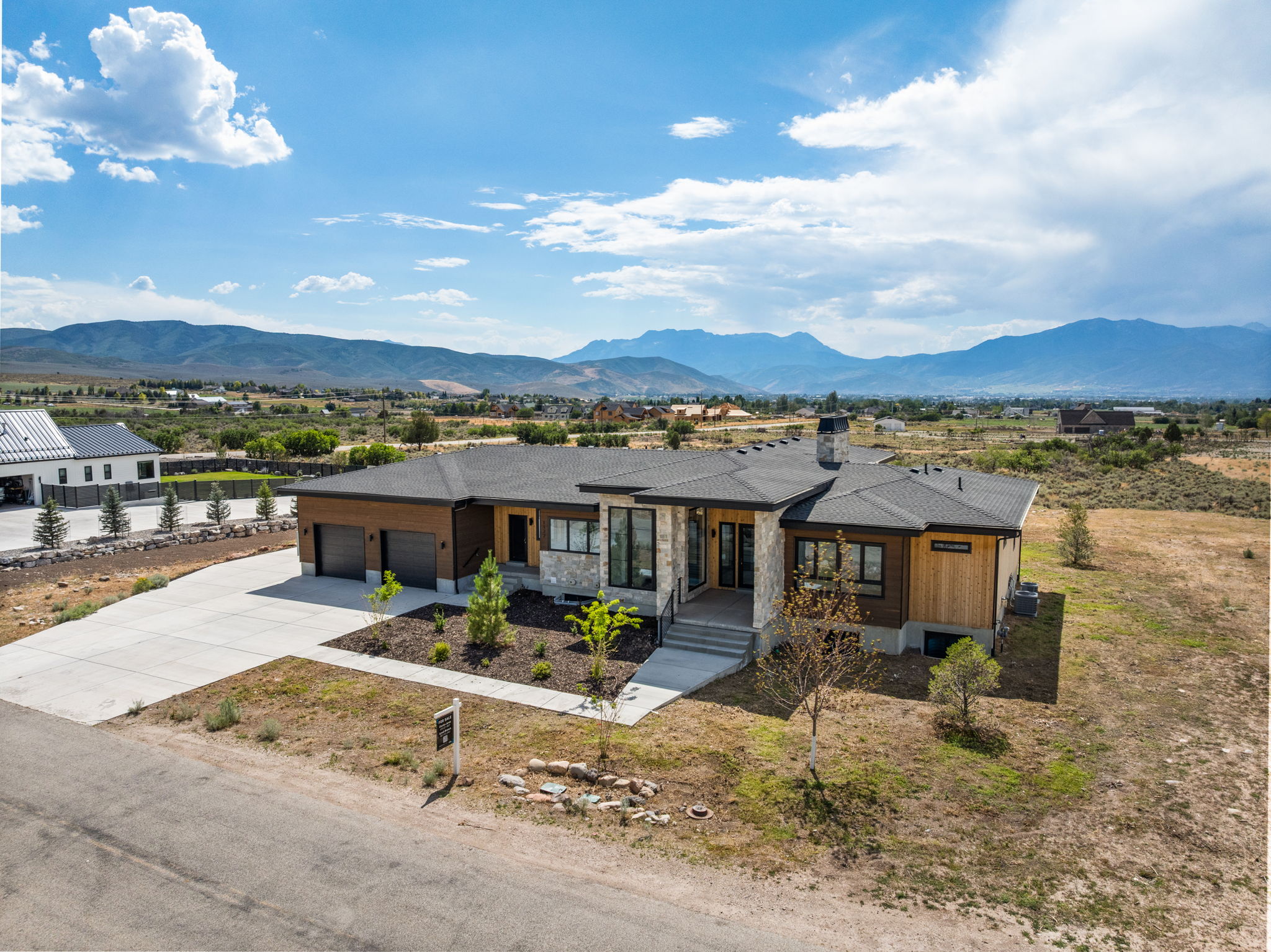 Modern ranch-style residence featuring a combination of stone veneer and wood siding, a two-car garage, and a concrete driveway