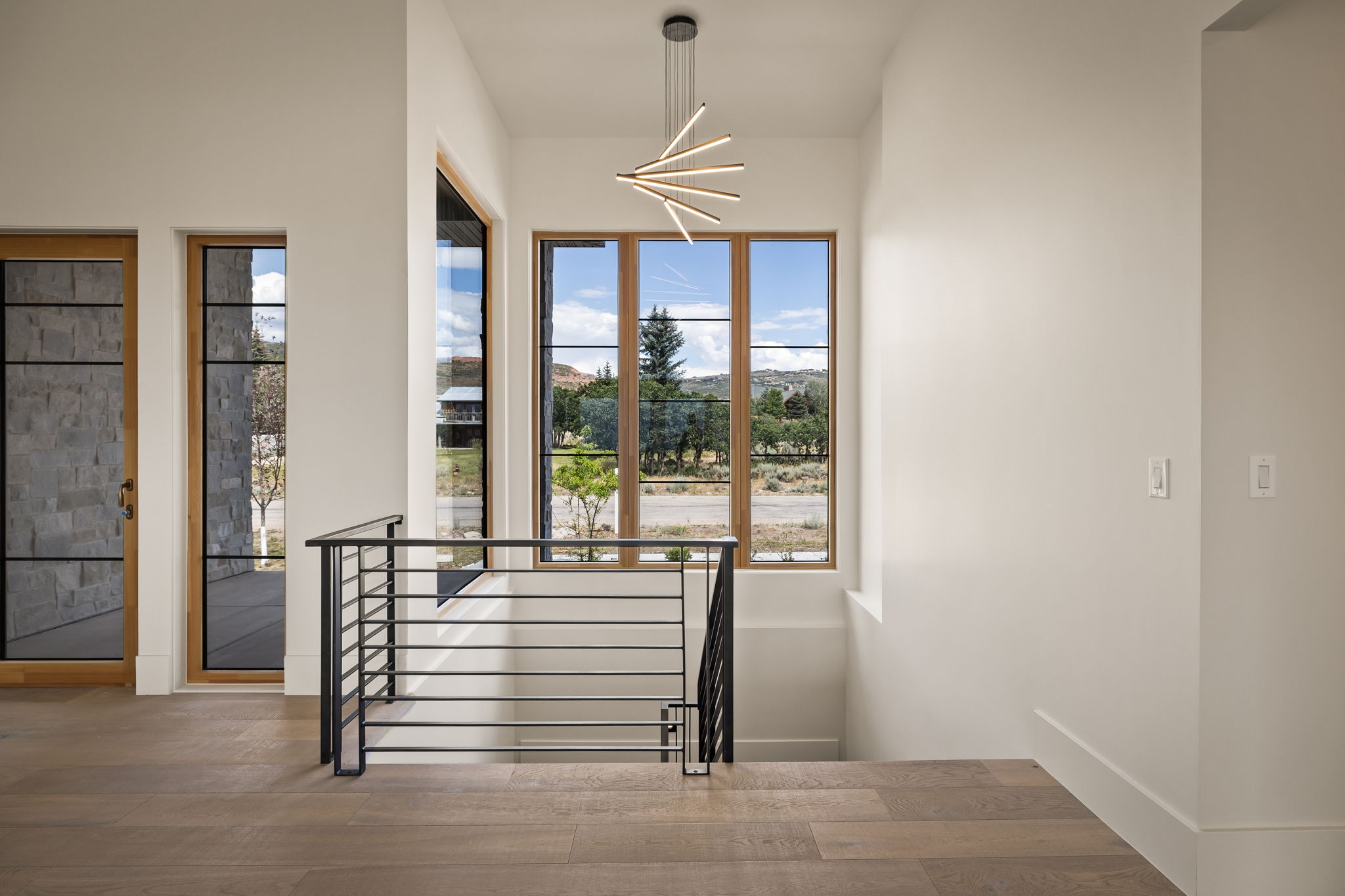 Architectural staircase featuring a linear chandelier, wood-finish flooring, and modern iron railings