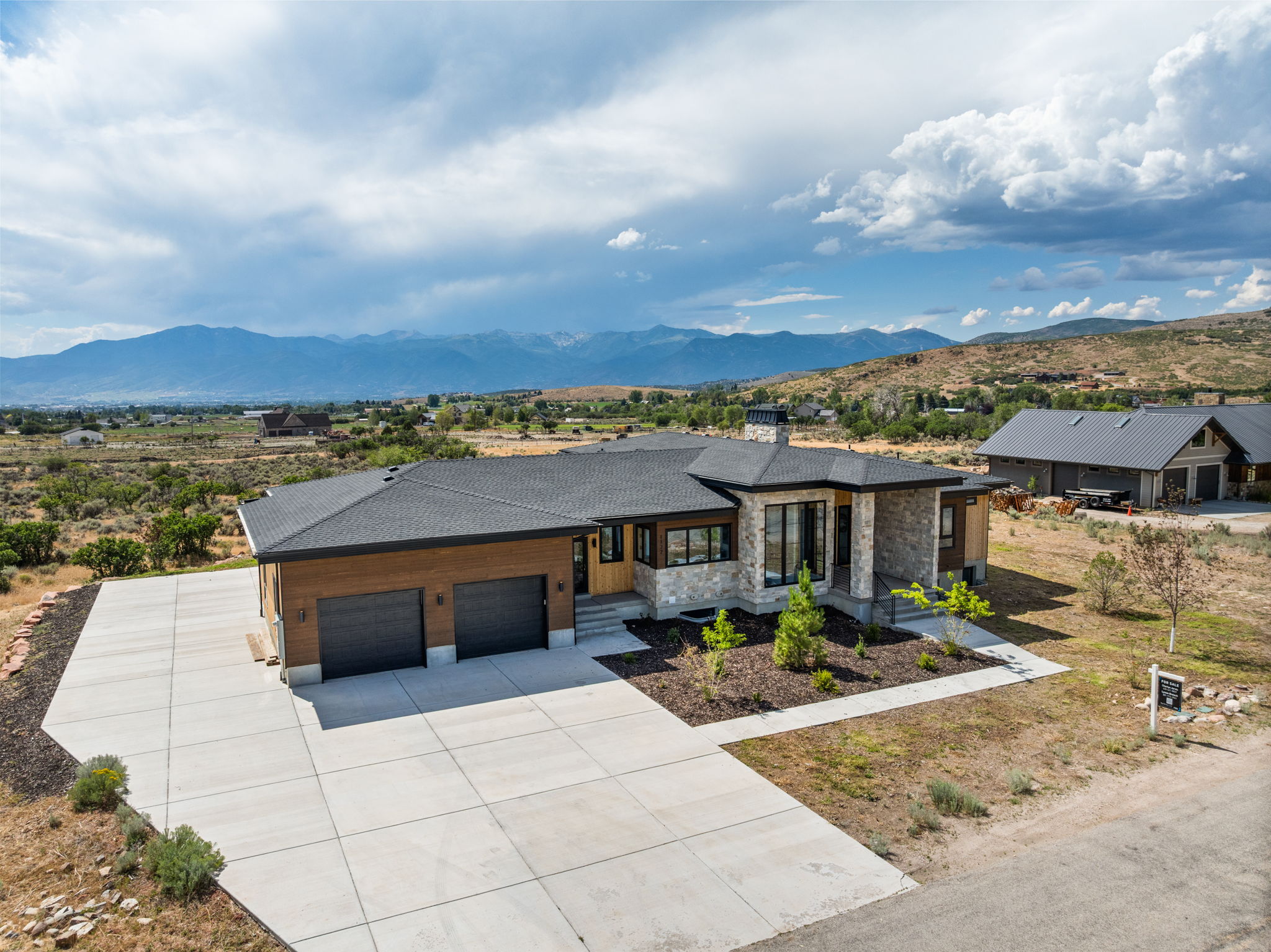 Contemporary residence featuring a stone and wood-tone exterior, an attached two-car garage, and a concrete driveway