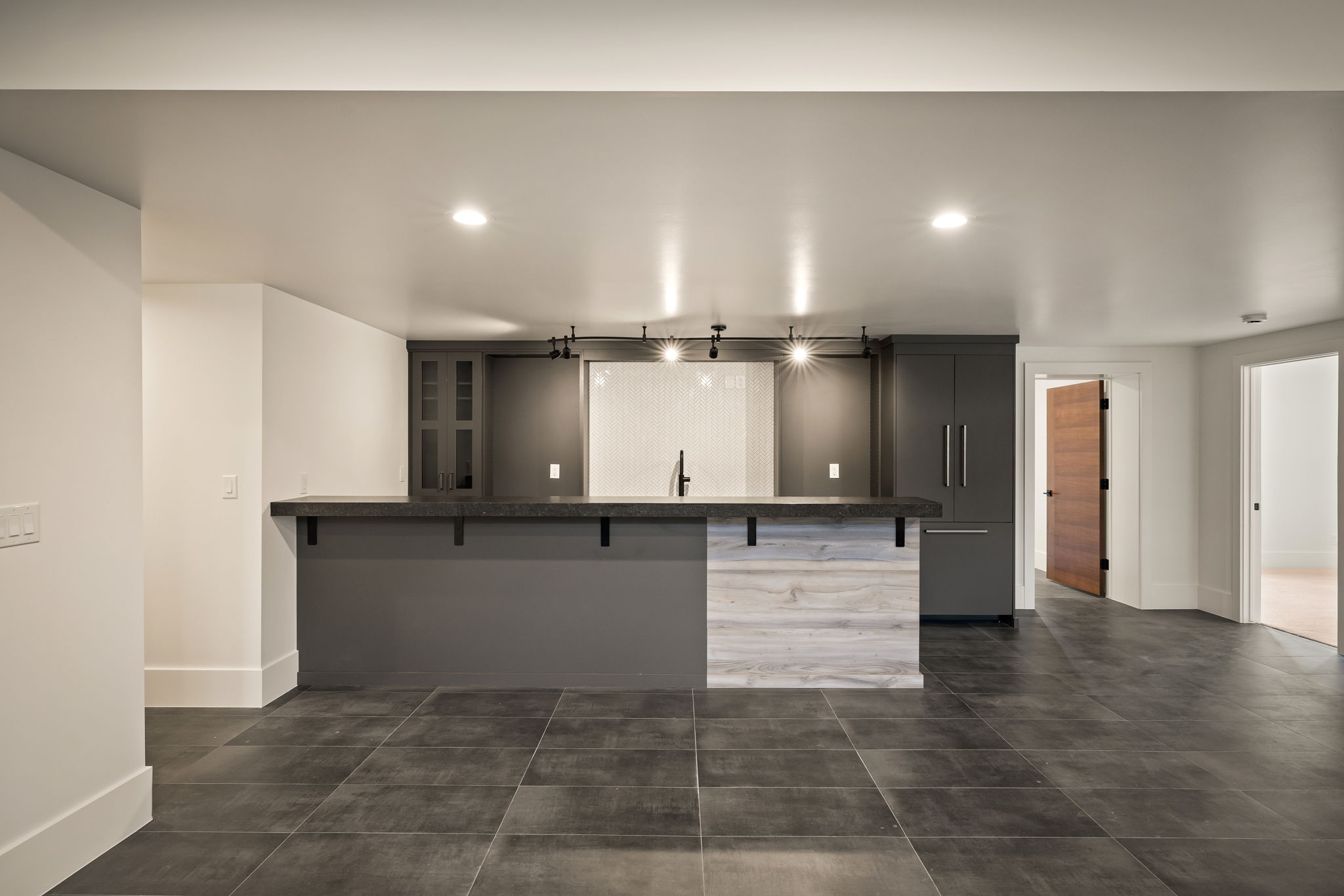 Modern wet bar featuring dark cabinetry, a solid surface countertop, white subway tile backsplash, and a built-in refrigerator