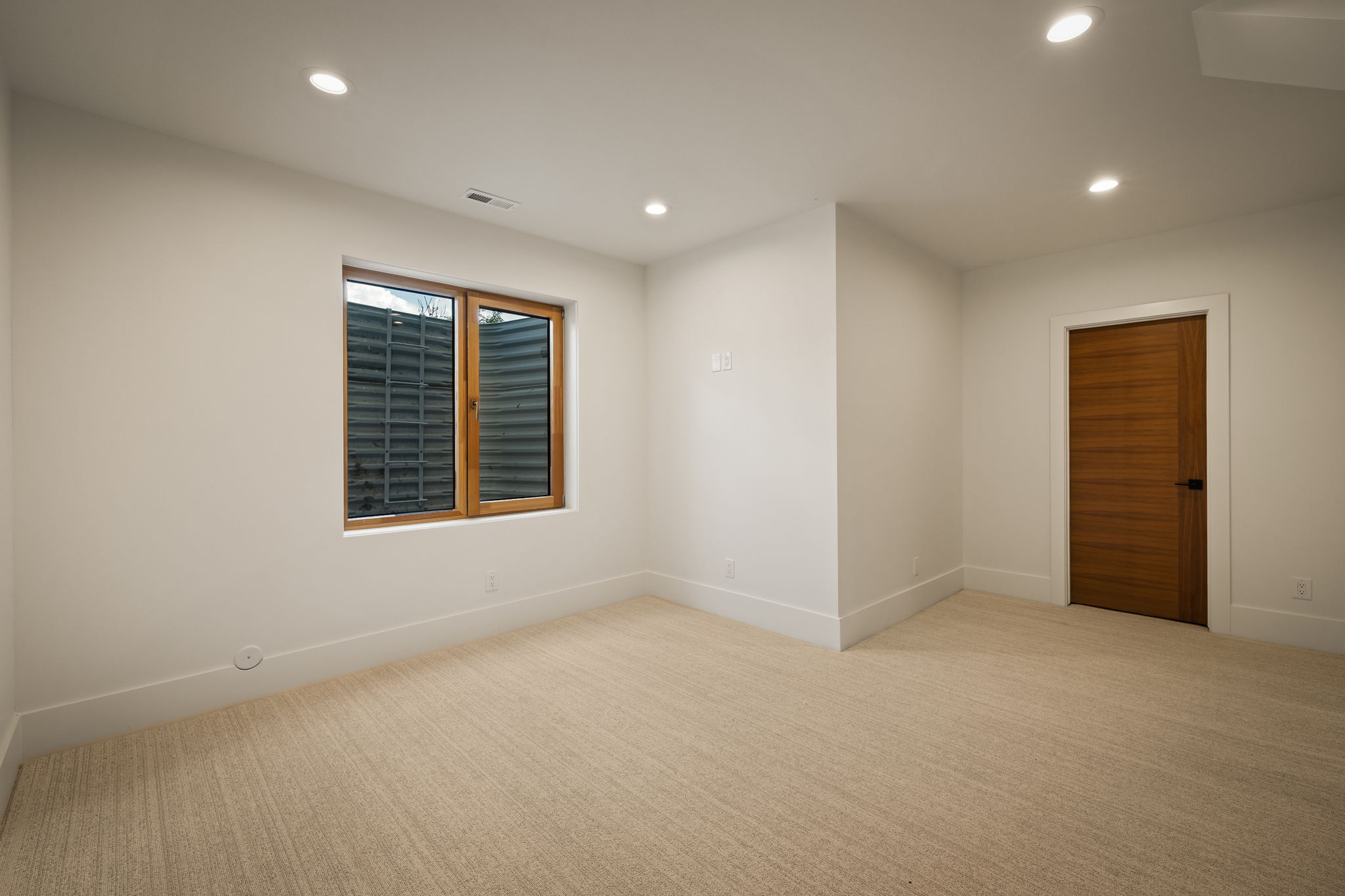 Carpeted room featuring recessed lighting, a window with a wood frame, and a solid wood door with a dark handle