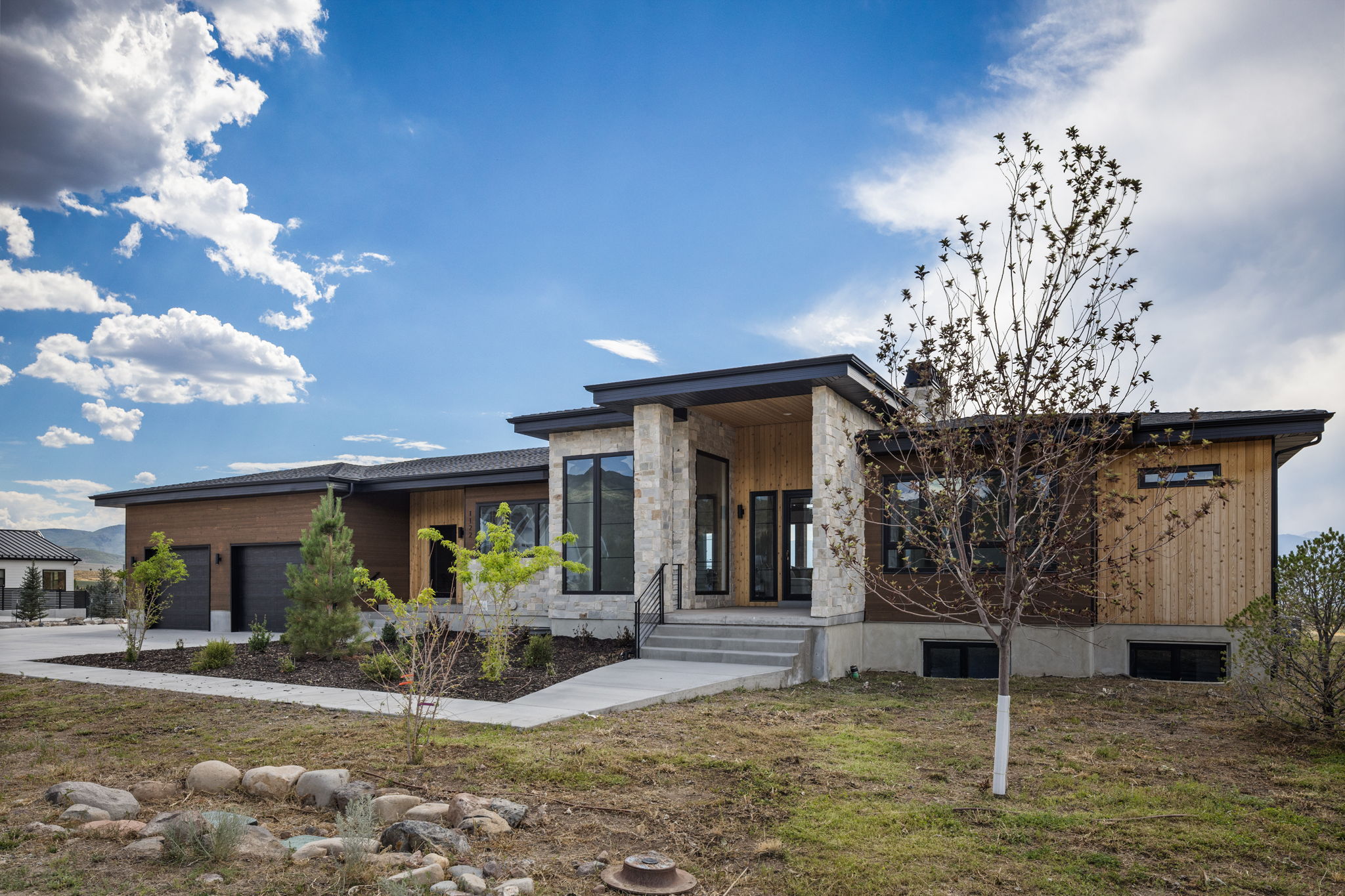 Modern architectural design featuring a prominent stone facade, wood siding, and large windows