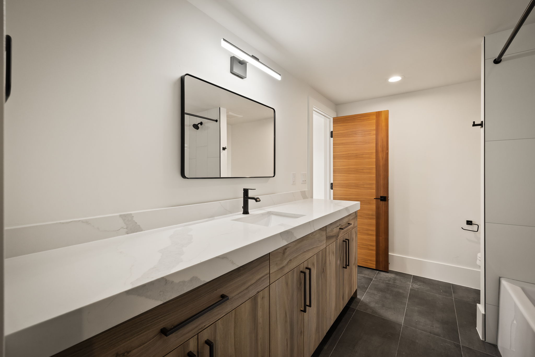 Contemporary bathroom featuring a wood-finish vanity with ample storage, a white countertop with integrated sink, and matte black fixtures