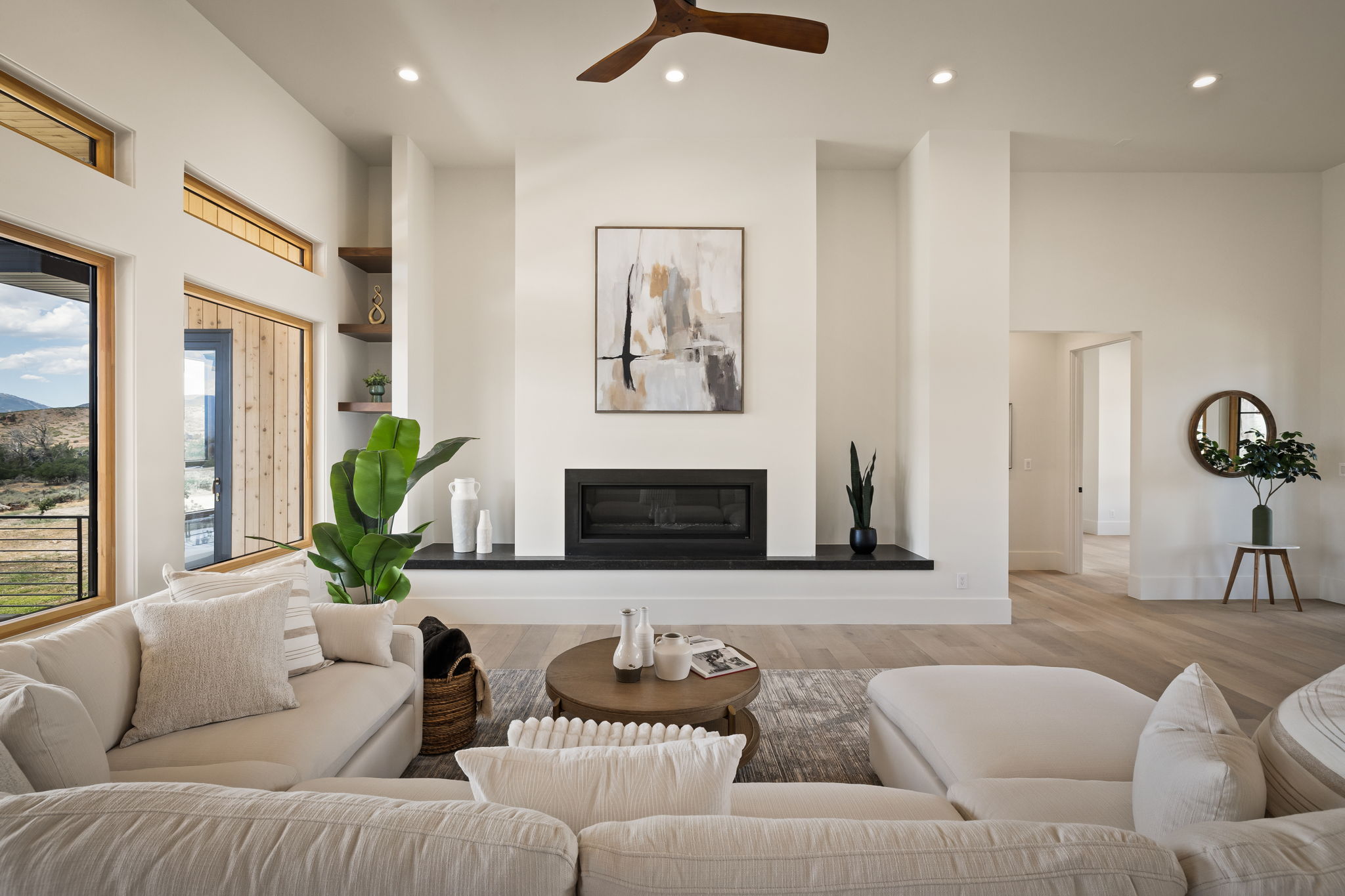 Spacious living area featuring high ceilings, a contemporary fireplace with a dark mantel, wood-finish flooring, and recessed lighting