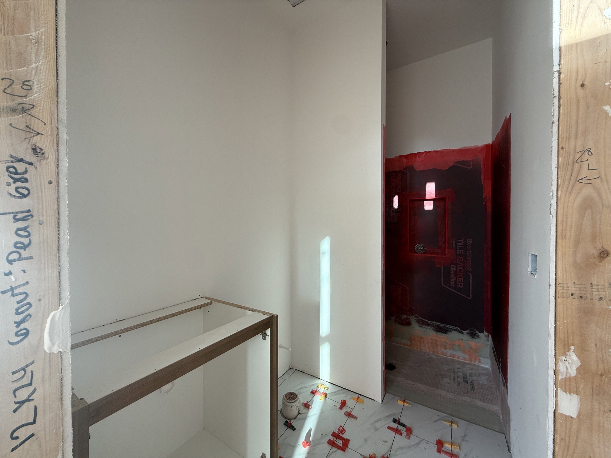 Bathroom under construction with white walls, a wood-finish vanity base, and large format floor tile