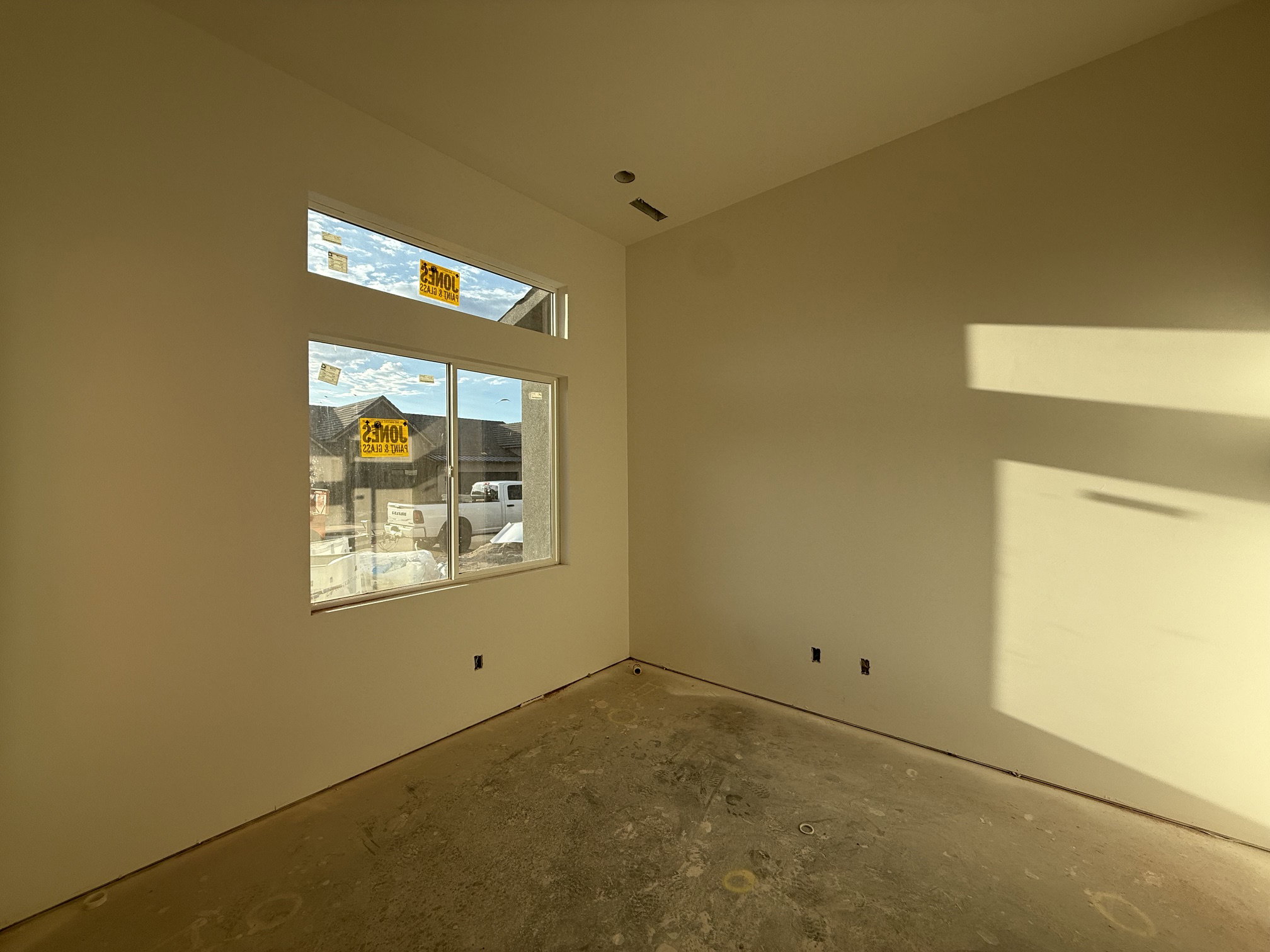 Unfinished interior space featuring a large window with an upper transom window, smooth walls, and concrete flooring