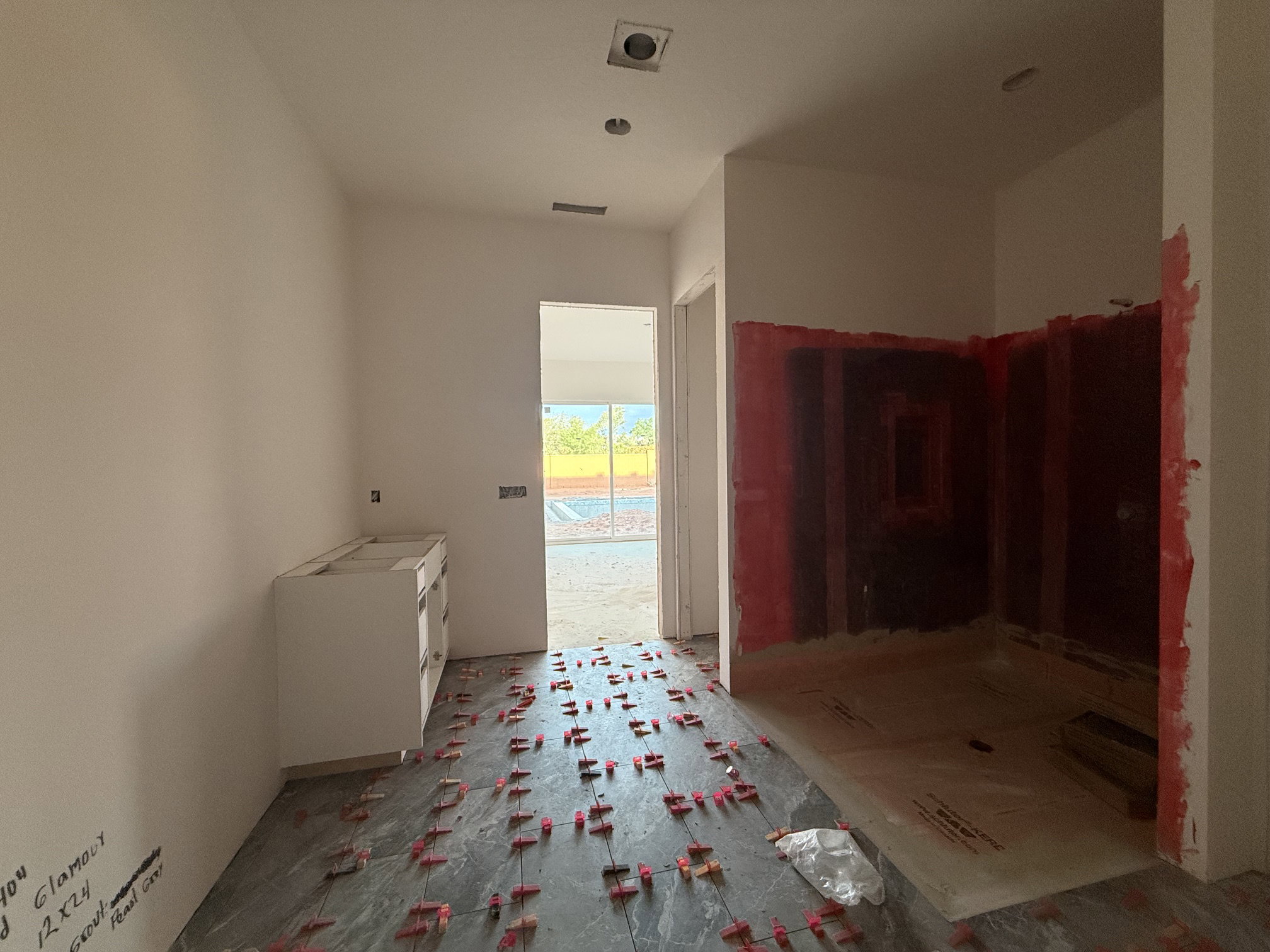 Interior space featuring a white vanity cabinet, dark gray tile flooring with leveling spacers, and a framed opening revealing an exterior area with a pool