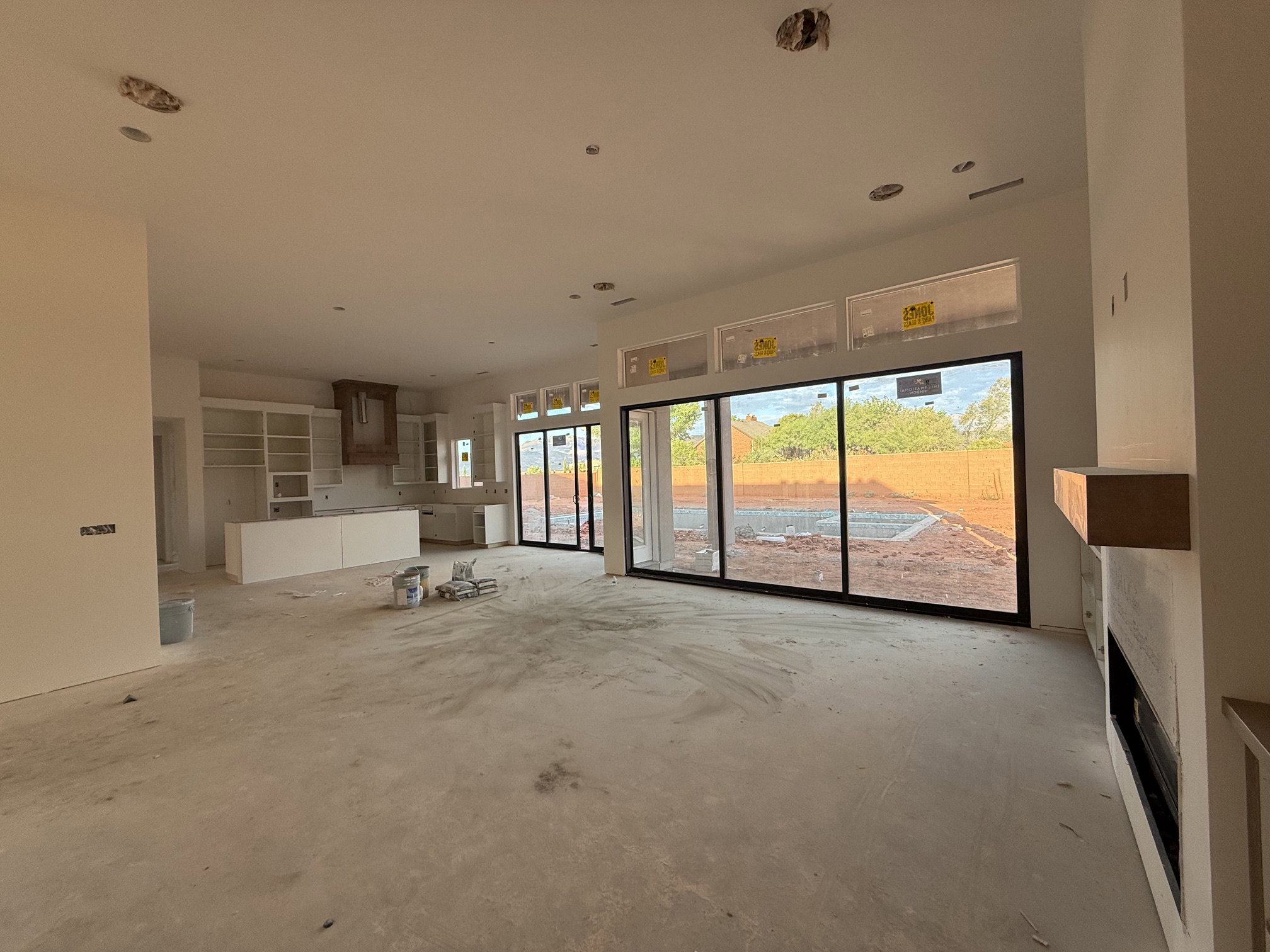Open concept interior featuring large sliding glass doors, transom windows, a built-in linear fireplace with a wood-finish mantel, and a kitchen area with white cabinetry and a wood-finish range hood