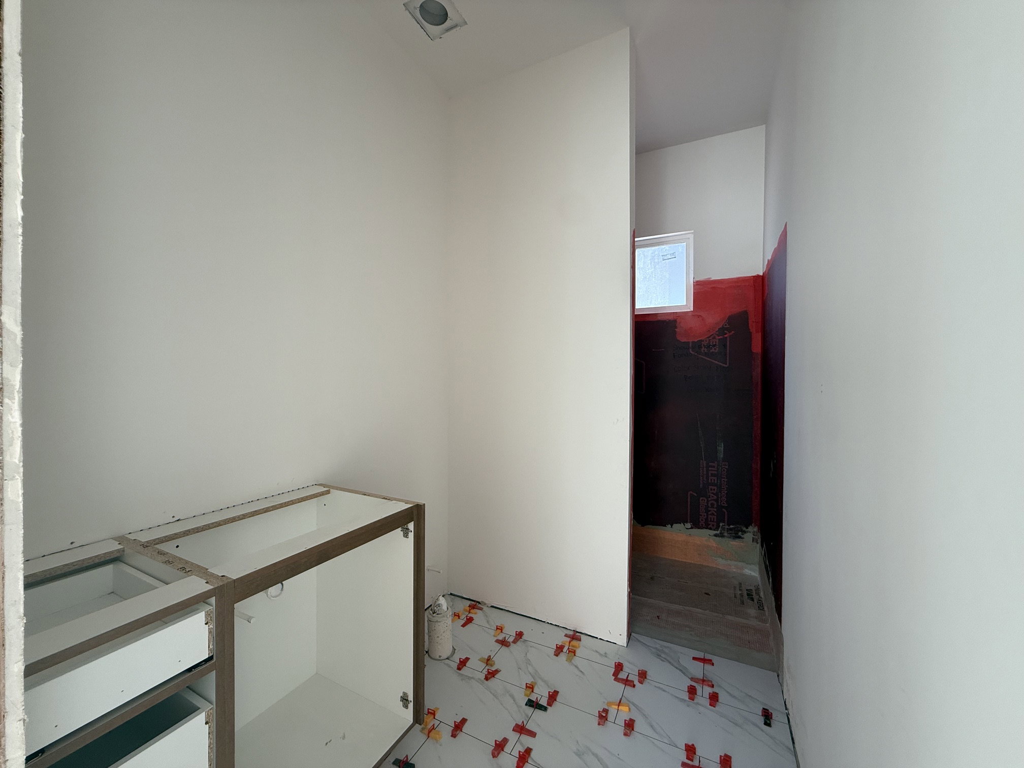 Bathroom under construction featuring a built-in vanity frame, recessed ceiling lighting, and a frosted window within the shower area