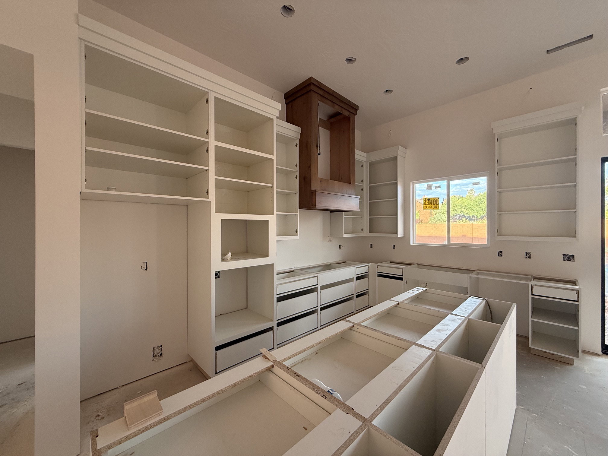 Expansive kitchen featuring white cabinetry, a large central island foundation, and a prominent wood-tone range hood