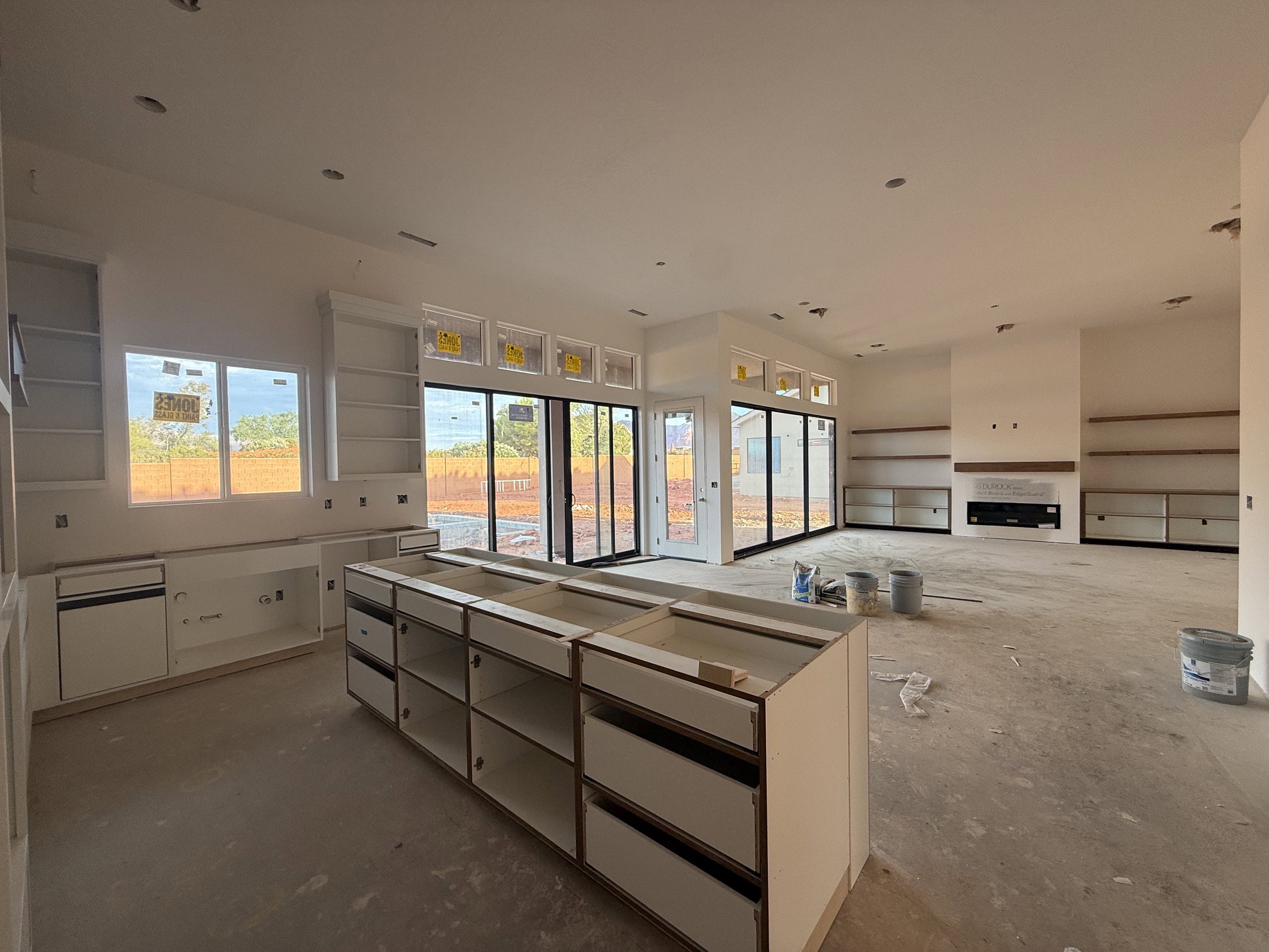 Expansive open-concept living space featuring a central island, extensive built-in cabinetry, large sliding glass doors, a modern fireplace with a mantel, and numerous recessed lights