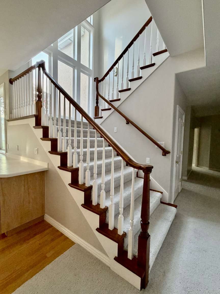 Two-story staircase featuring wood newel posts, handrails, and treads with white balusters