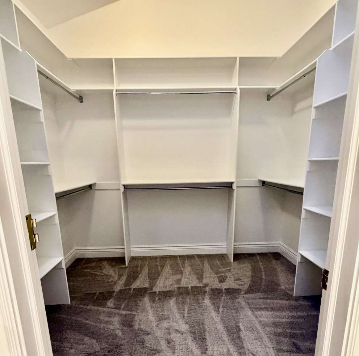Walk-in closet featuring built-in shelving, multiple hanging rods, white cabinetry, and gray carpet flooring
