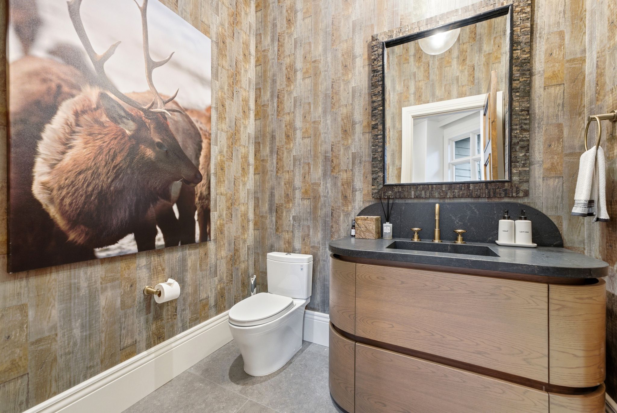 Powder room featuring a curved wood-finish vanity with an integrated sink, dark stone countertop, and brass fixtures