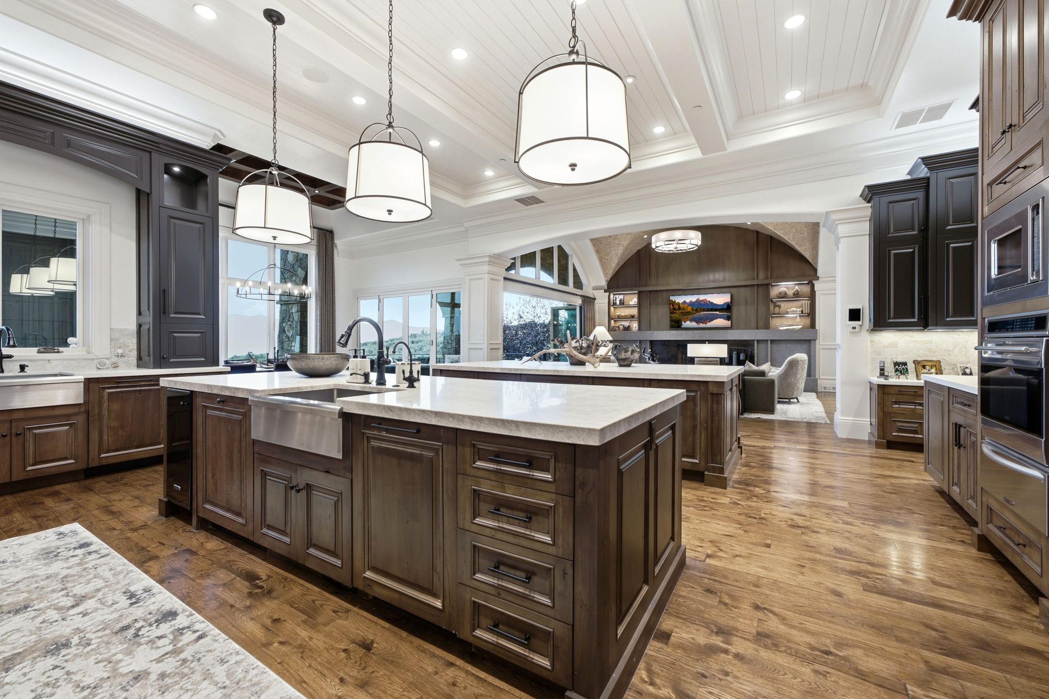 Gourmet kitchen featuring two large islands with white countertops and sinks, wood-finish flooring, two-tone cabinetry, and three pendant light fixtures