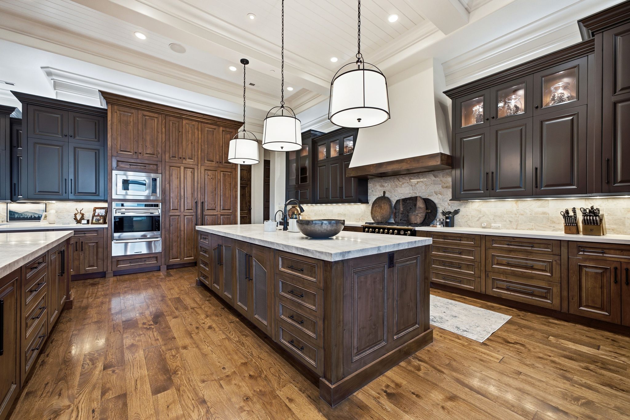 Gourmet kitchen featuring a substantial central island with integrated storage, wood-finish flooring, two-tone cabinetry, professional-grade stainless steel appliances, and coffered ceiling details