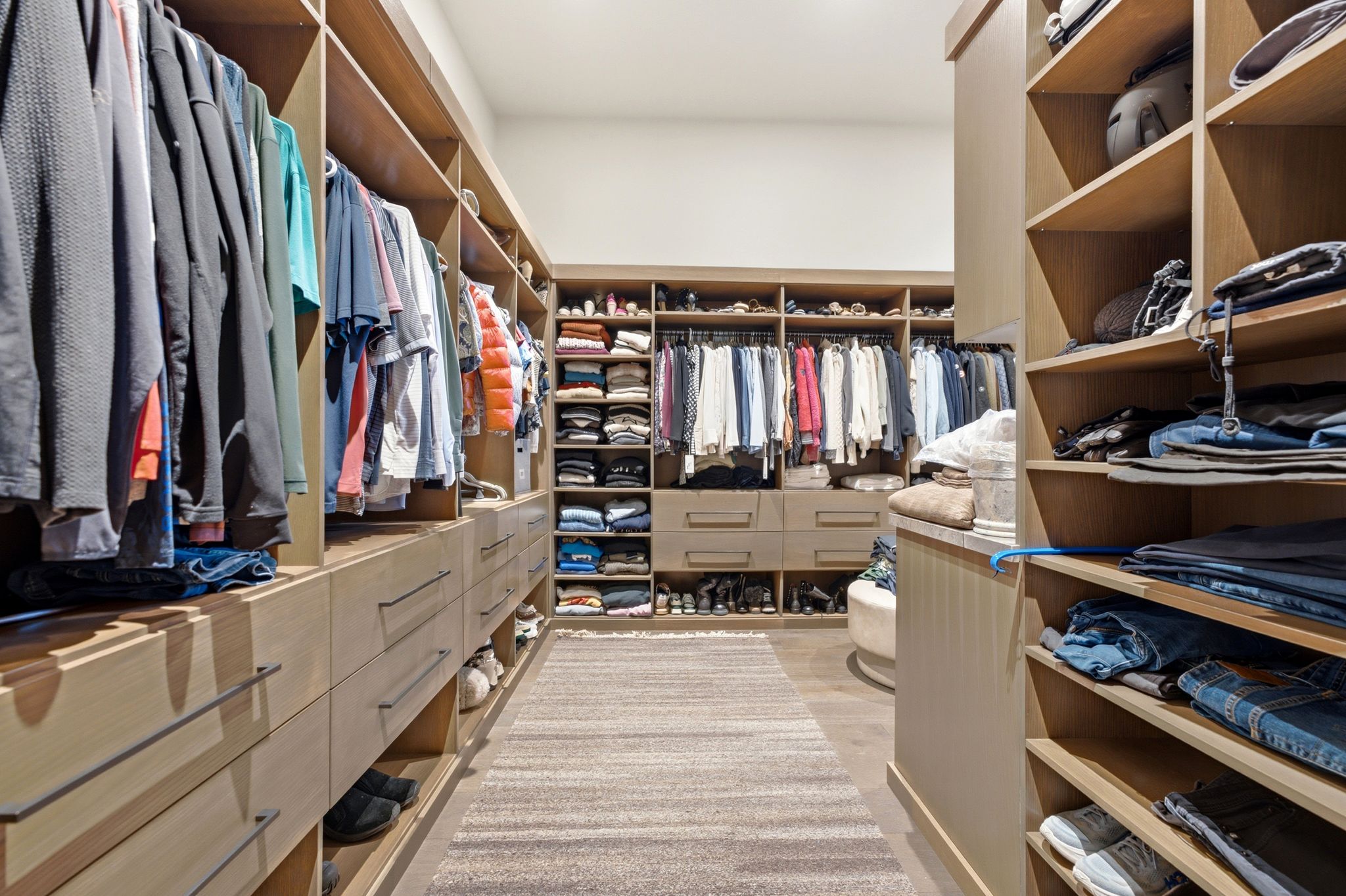 Custom-designed closet with extensive wood-finish shelving, multiple hanging rods, built-in drawer storage, and a central island with countertop