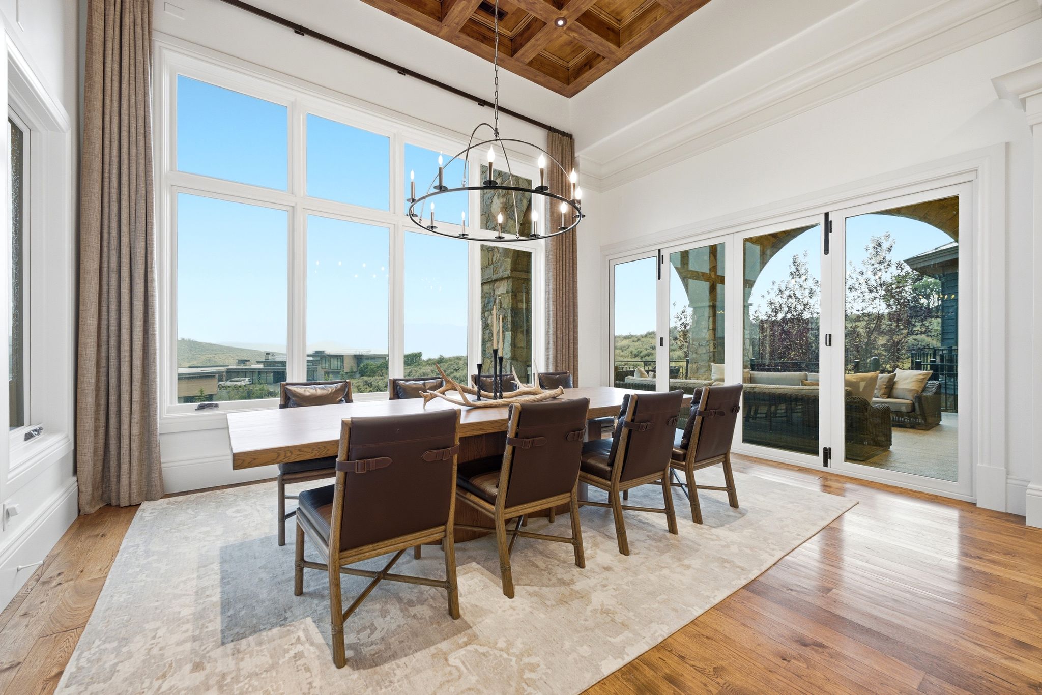 Dining area featuring expansive windows, wood-finish flooring, a coffered ceiling, and direct access to an outdoor patio through arched glass doors