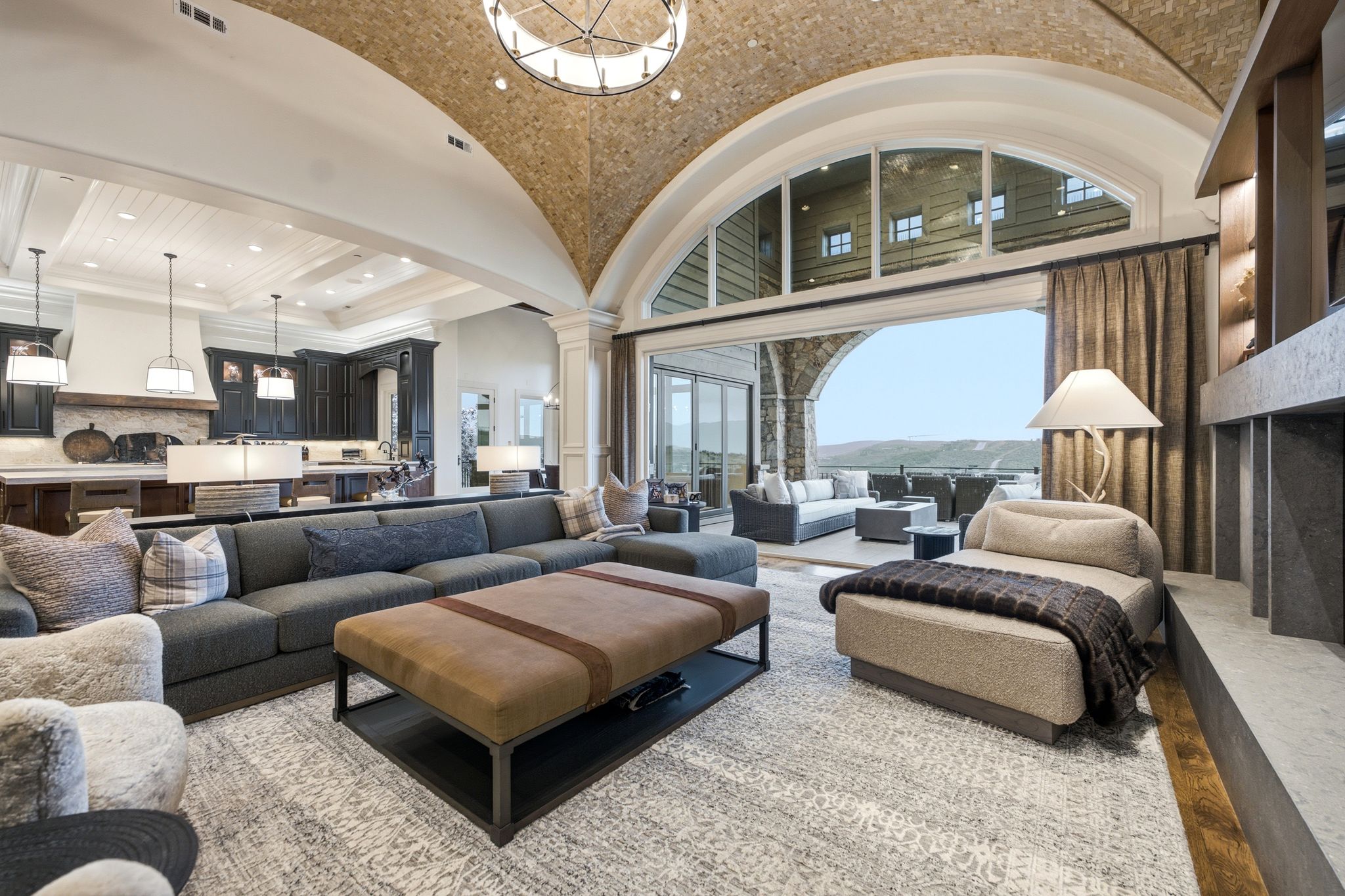 Spacious living area featuring a vaulted ceiling with exposed stonework, a large arched window, a built-in fireplace with display shelving, and an expansive sliding glass door opening to an outdoor patio