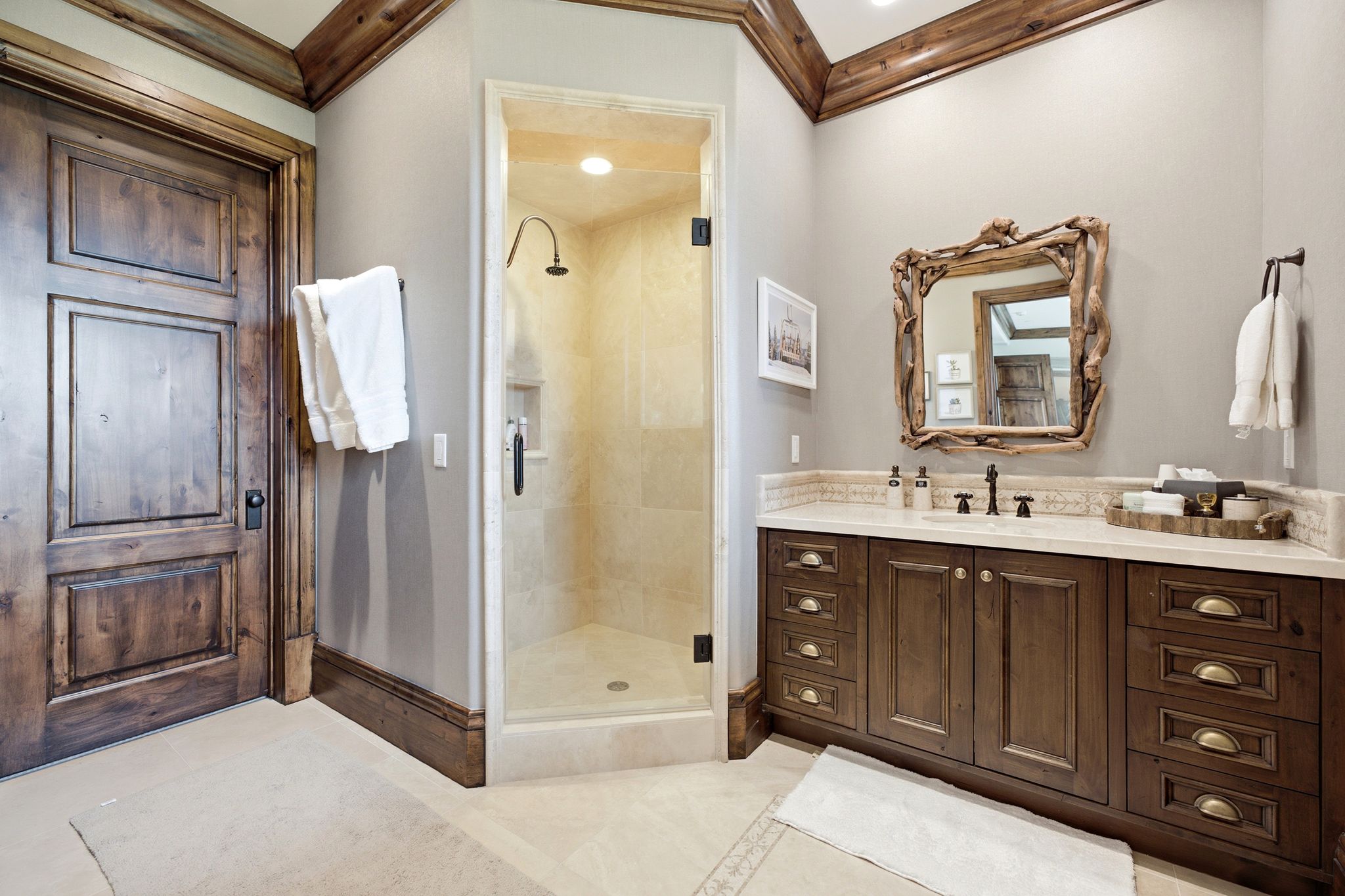 Bathroom featuring a wood-finish vanity with a light-toned countertop, a frameless glass shower enclosure with a rain showerhead, a large wood-framed mirror, and wood-finish trim accents