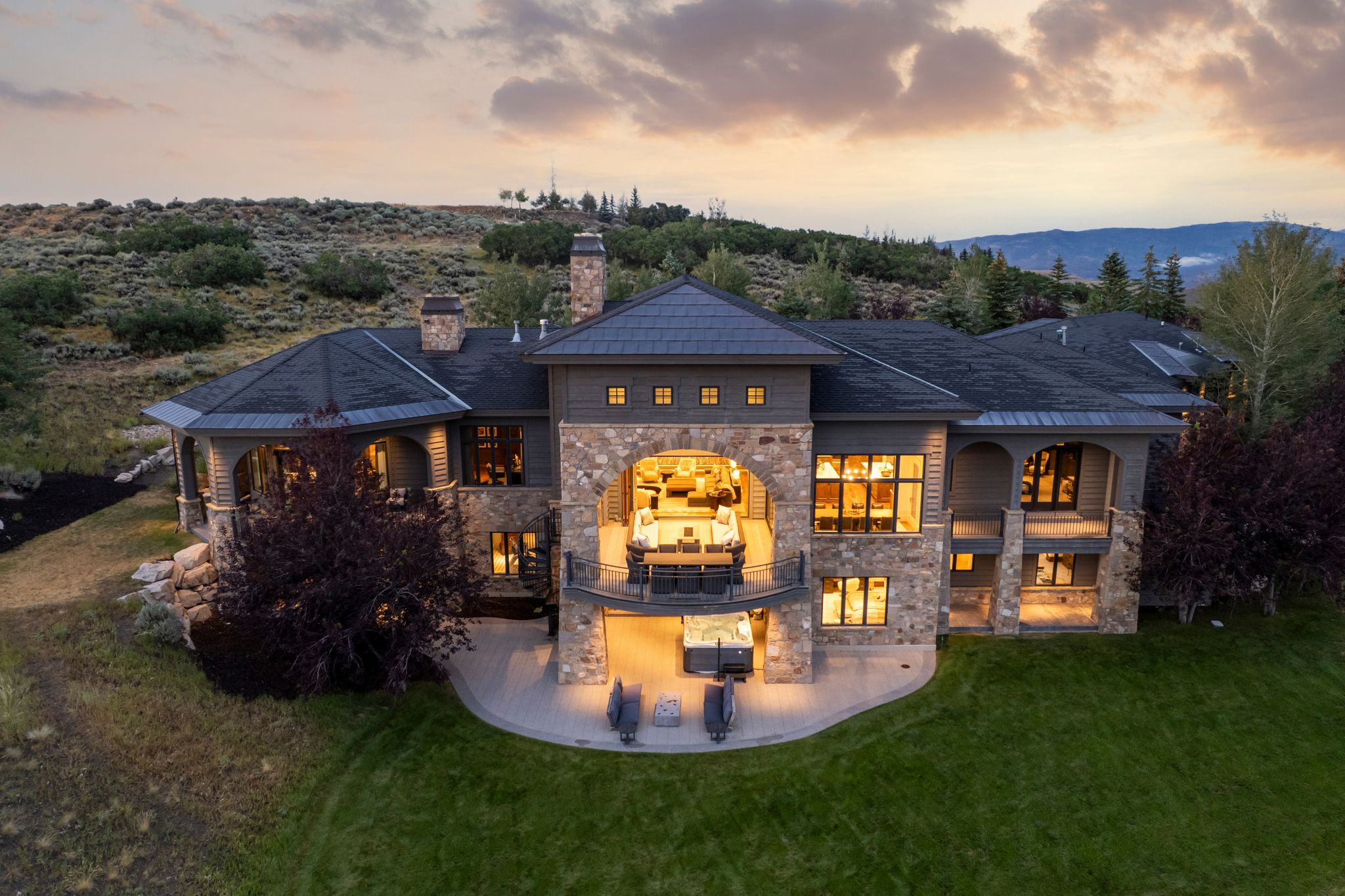 Expansive residence featuring stone and siding exterior, multiple balconies, and a lower-level patio with a spa