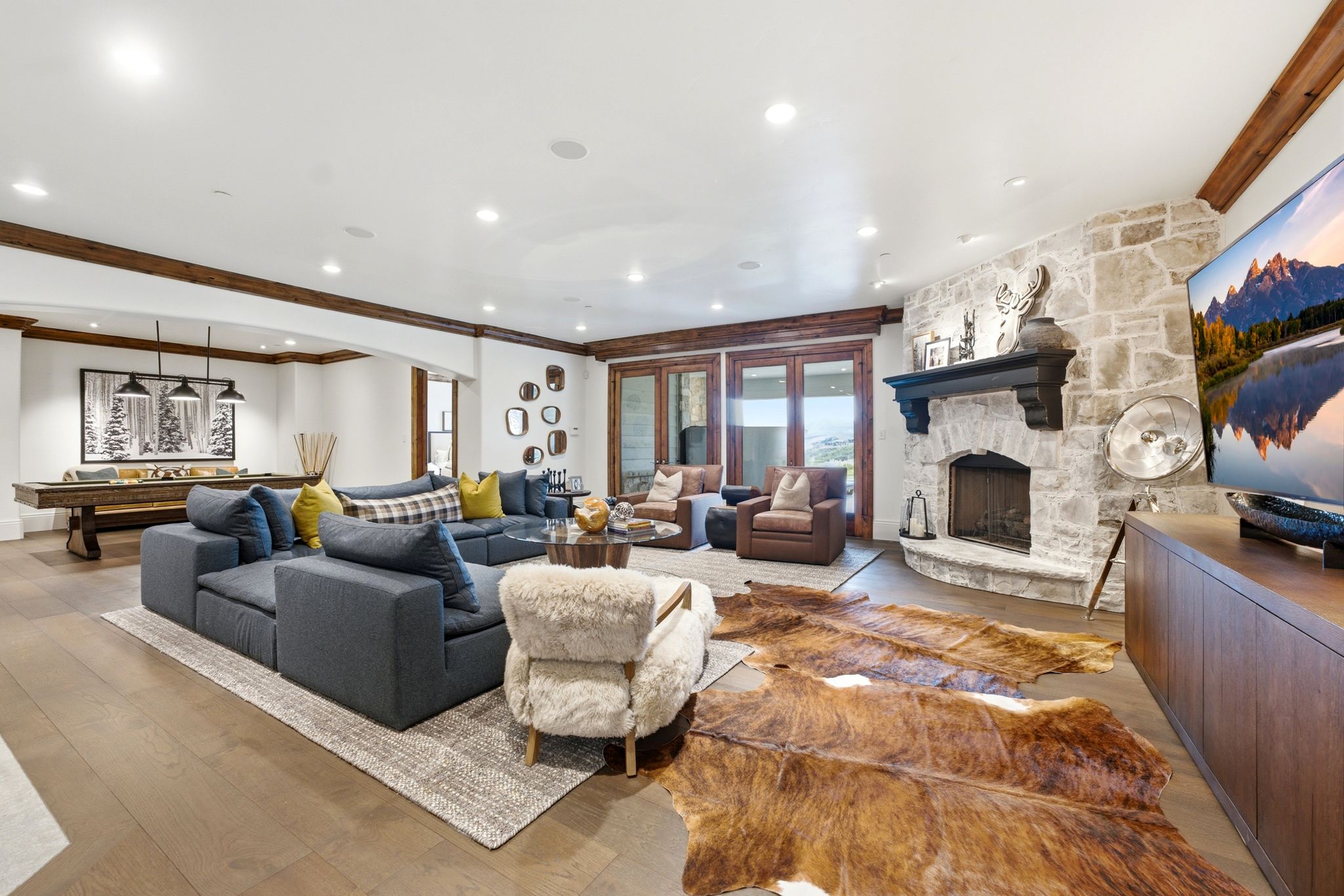 Spacious gathering room featuring wood-finish flooring, a stone-clad fireplace with a dark wood mantel, and exposed wood beam accents