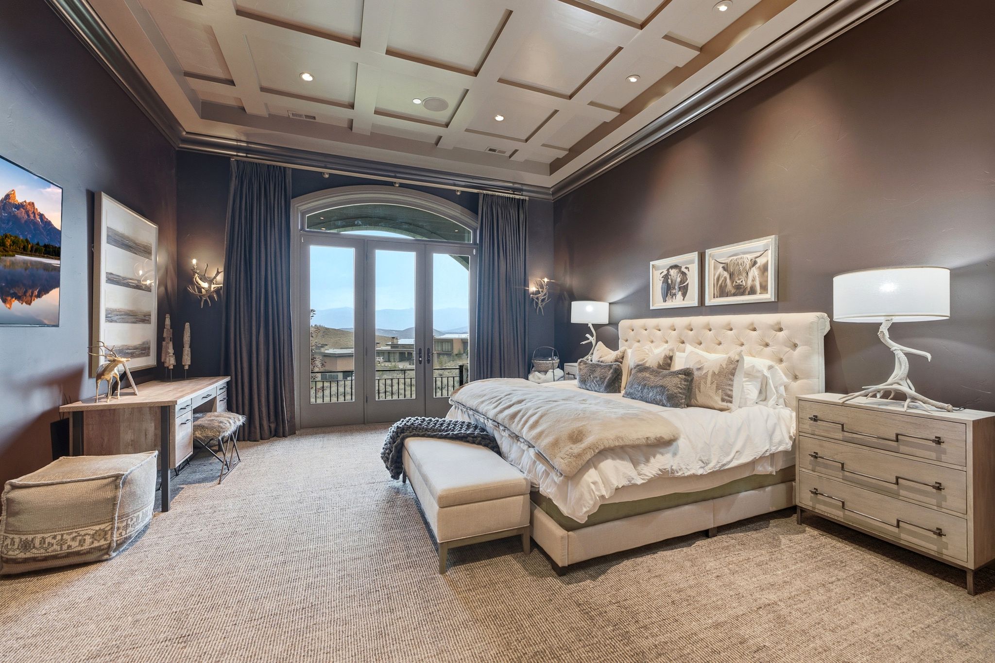 Arched French doors opening to an exterior balcony, coffered ceiling, recessed lighting, wall sconces, and neutral tone carpeting