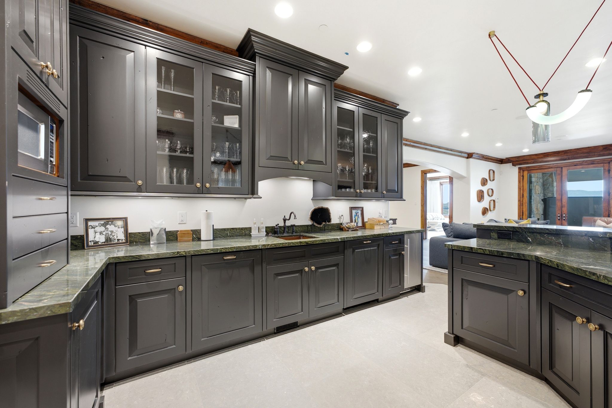 Kitchen featuring dark-toned cabinetry with glass-front uppers, green-hued countertops, under-cabinet lighting, and stainless steel appliances
