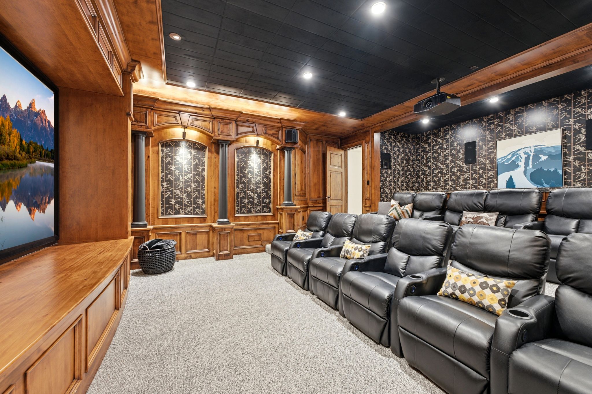 Dedicated home theater featuring tiered seating, built-in media console, wood-paneled walls with decorative architectural elements, recessed lighting, and a ceiling-mounted projector