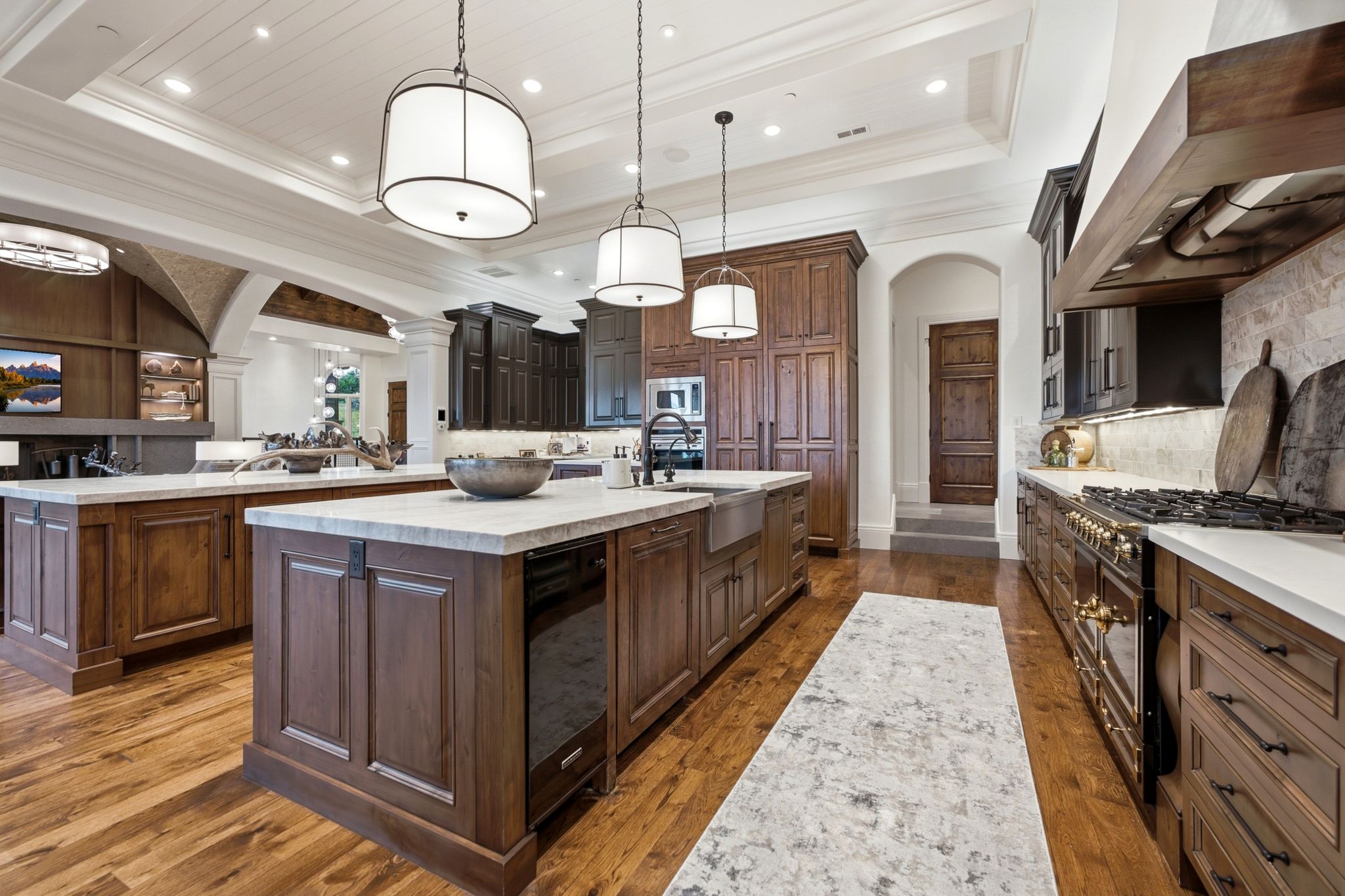 Gourmet kitchen featuring two substantial islands, professional-grade range, custom wood cabinetry, wood-finish flooring, and coffered ceilings