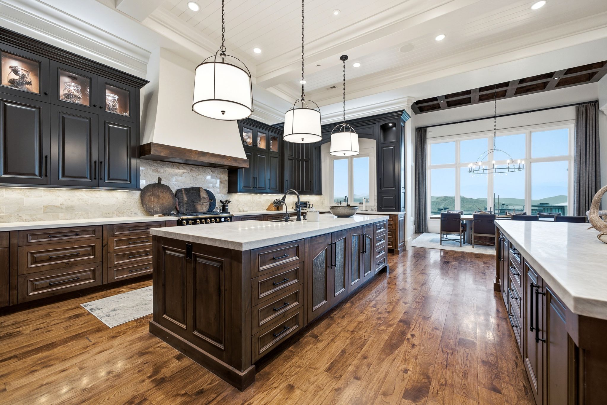 Gourmet kitchen featuring a large central island with a light-toned countertop, rich wood-finish flooring, and dark cabinetry