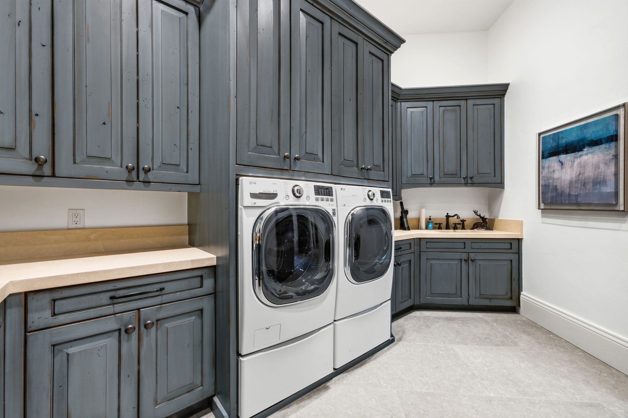 Laundry room featuring extensive distressed cabinetry, light-toned countertops, tile flooring, and integrated washer and dryer units