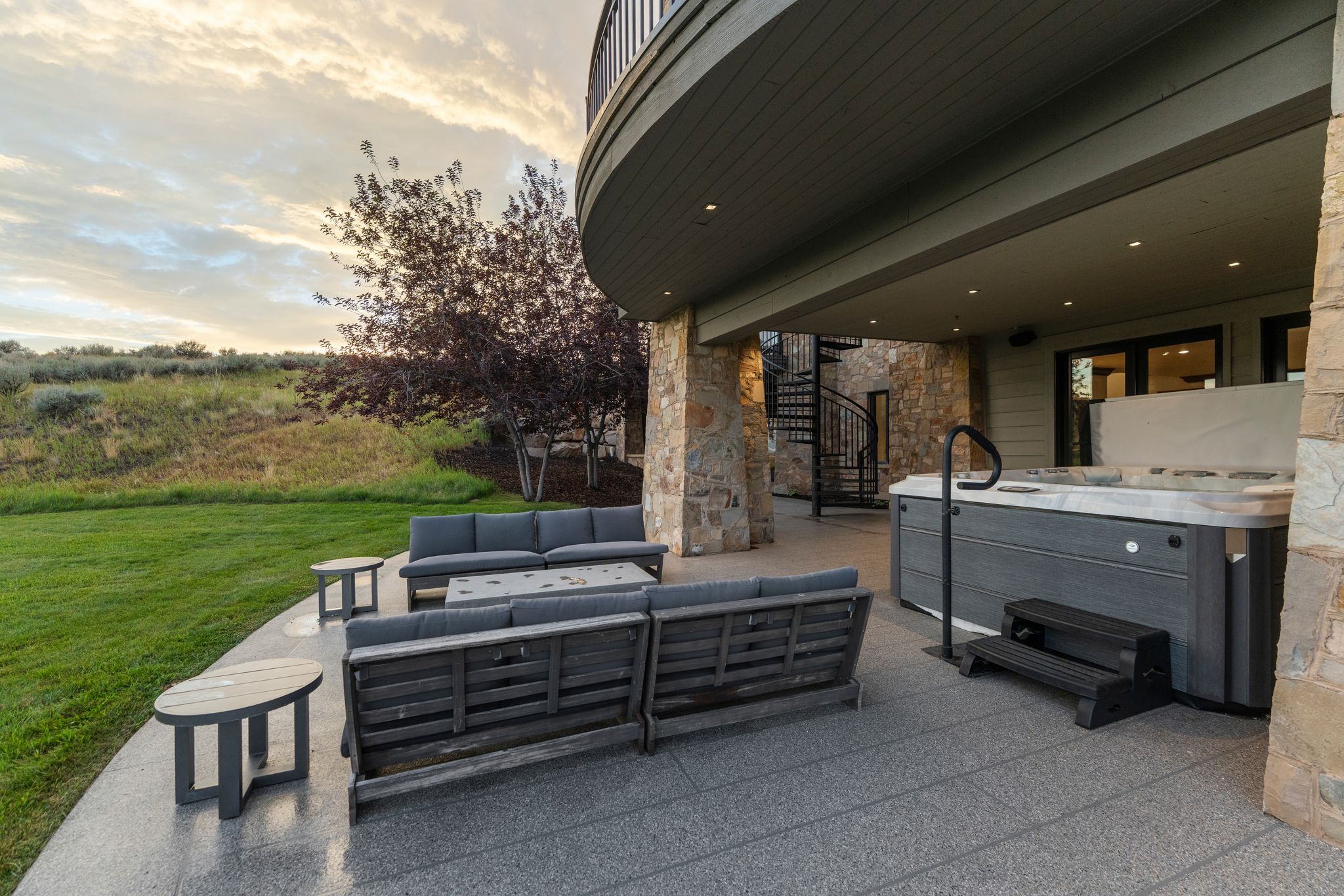 Expansive patio featuring a built-in spa, overhead lighting, spiral staircase, and stone column accents