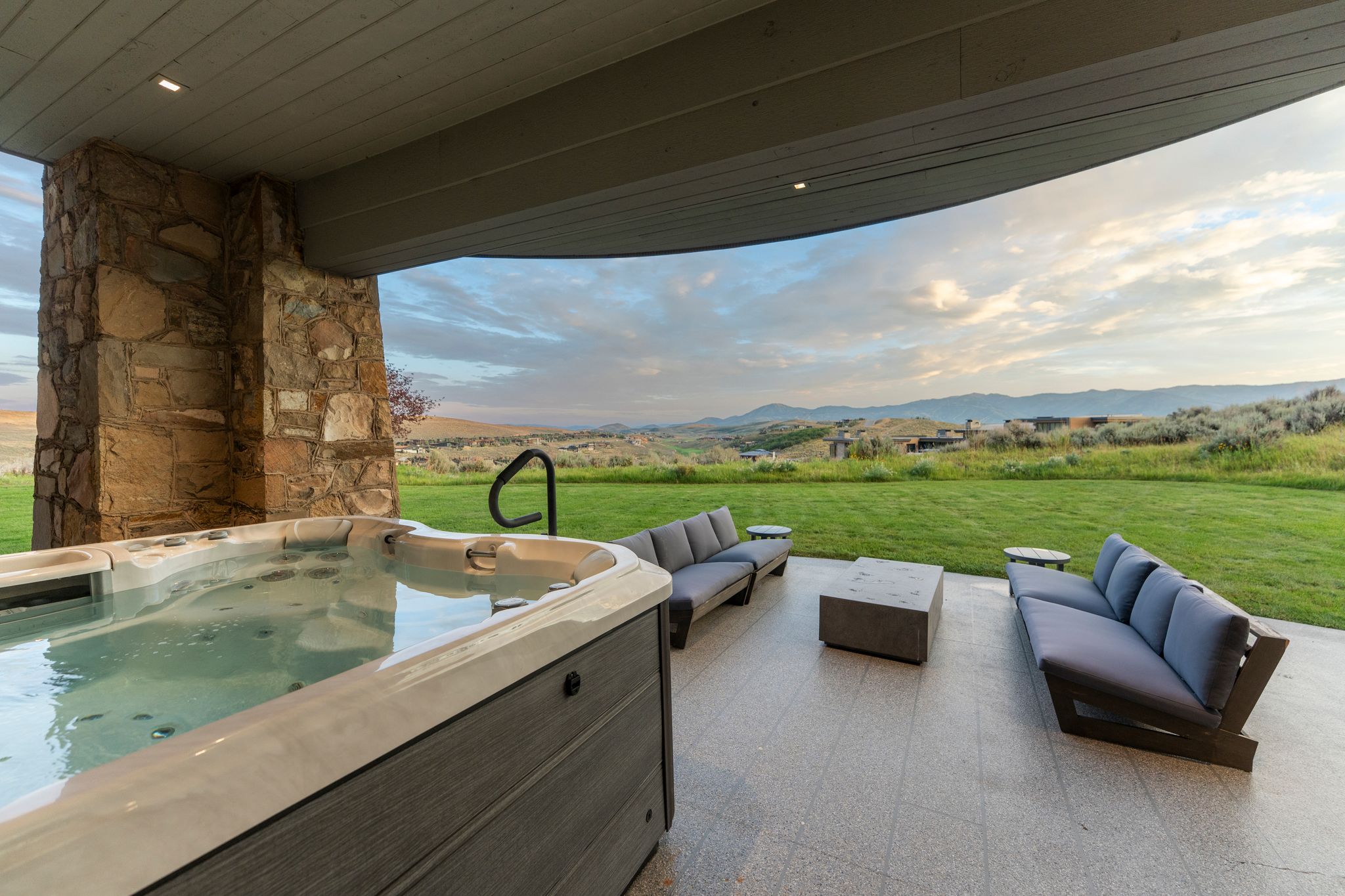 Outdoor covered patio featuring a built-in hot tub, stone-clad architectural elements, and a concrete paver surface