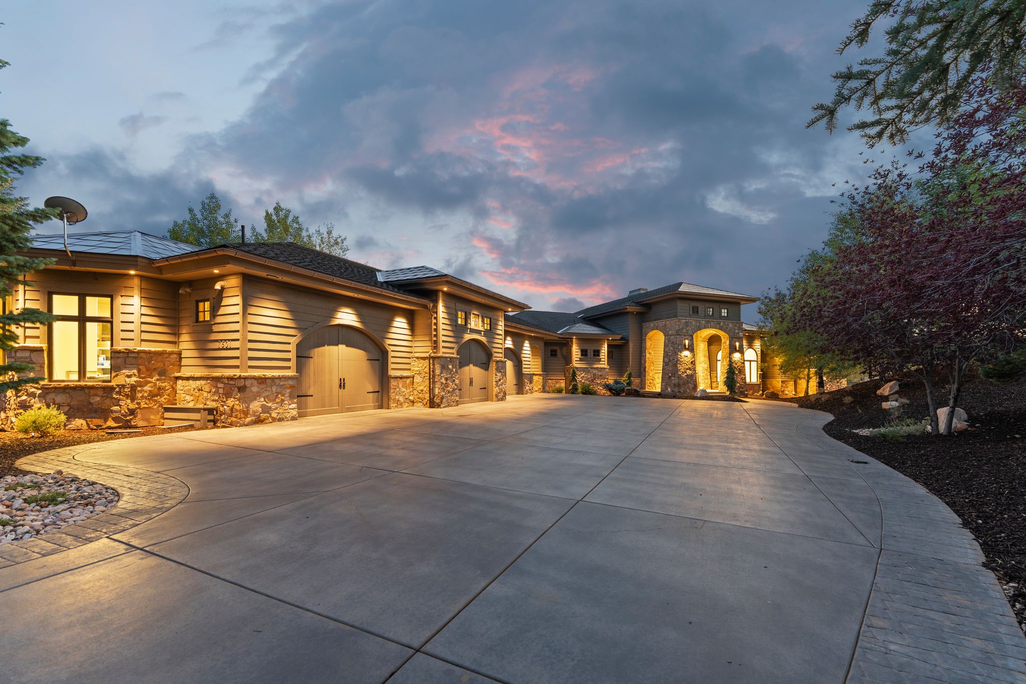 Expansive concrete driveway leading to a stone and wood-sided architectural style