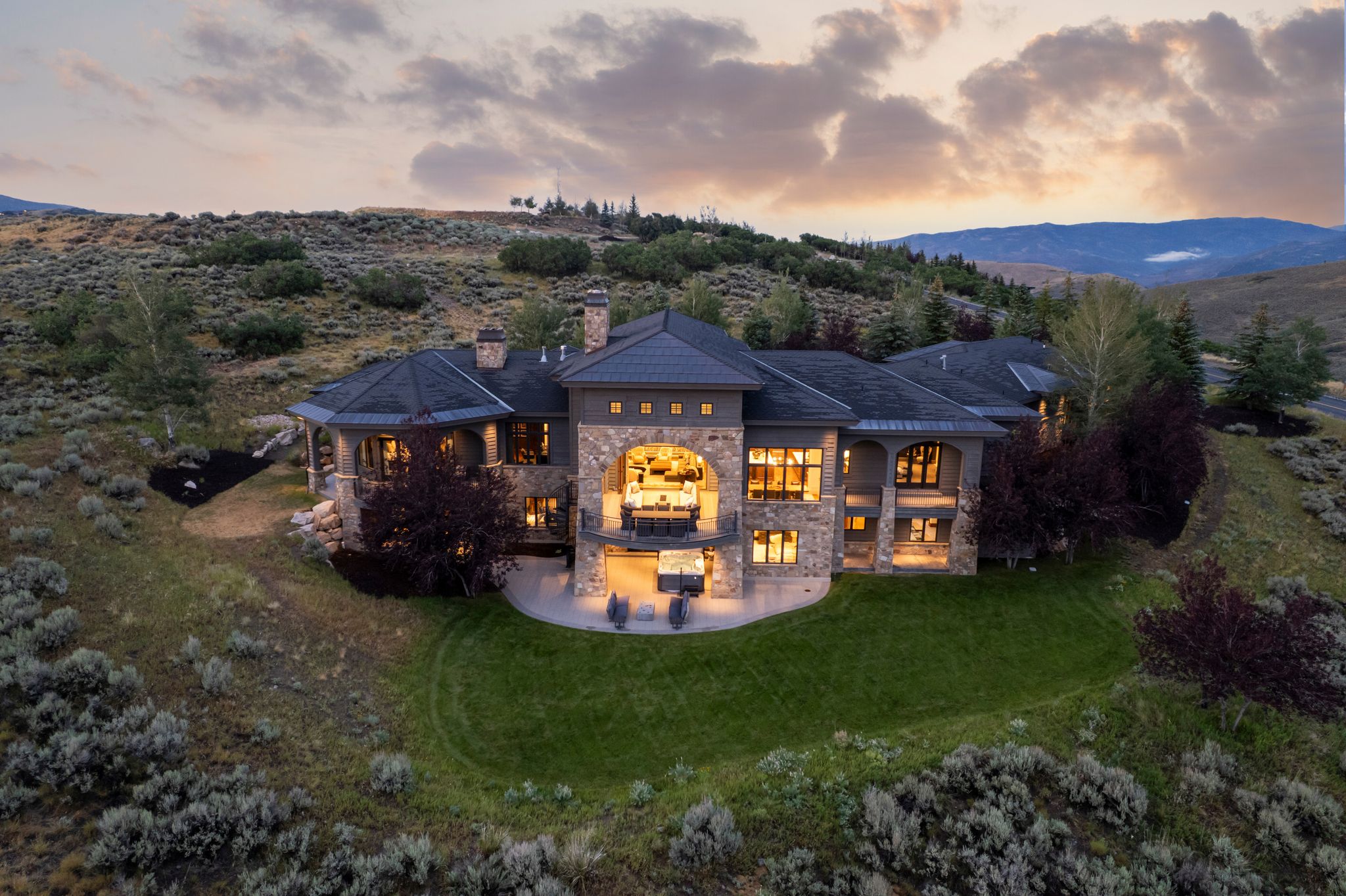 Expansive custom residence featuring a stone and stucco exterior, multiple covered balconies, a spacious patio, and a manicured lawn