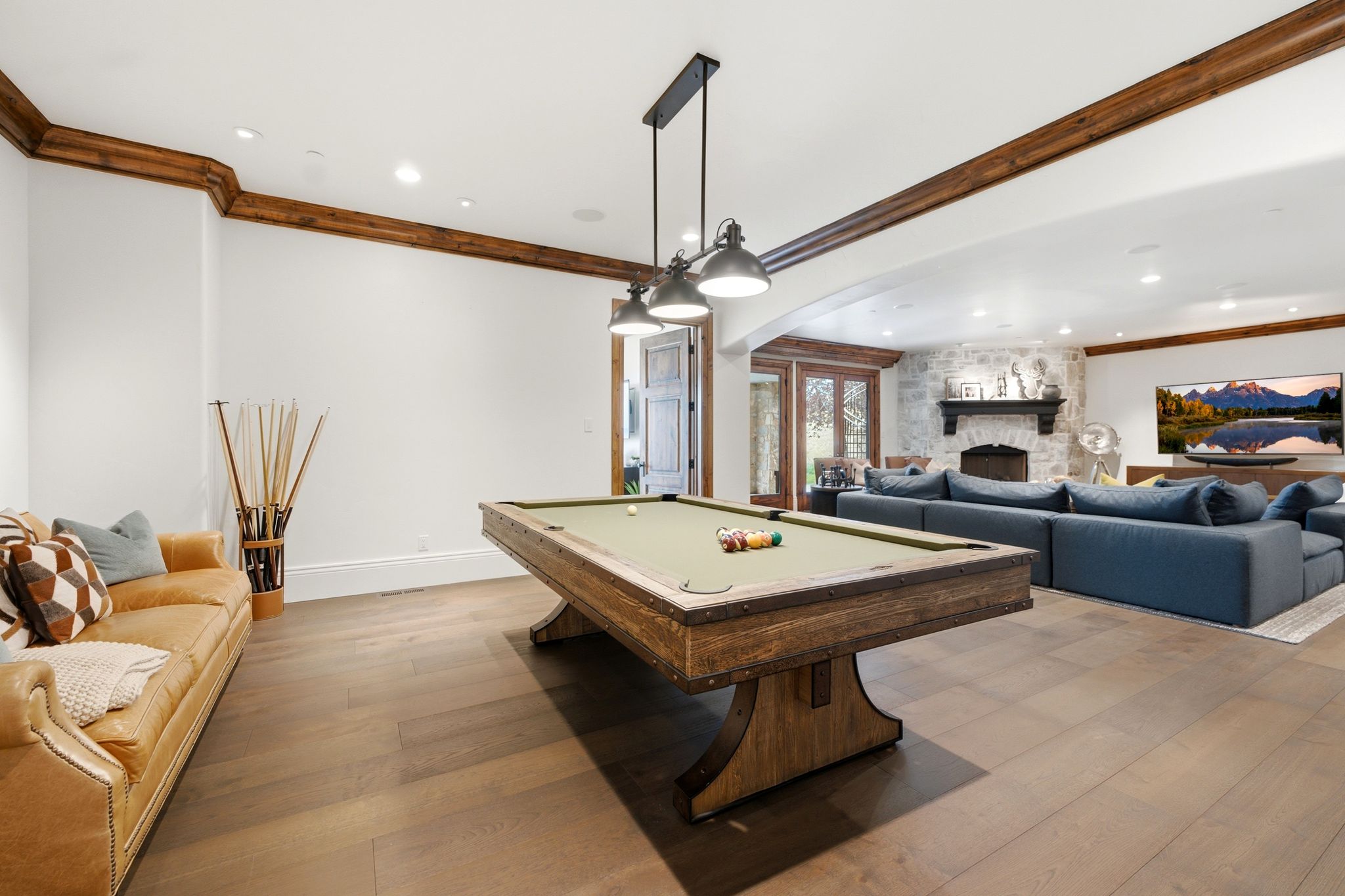 Spacious recreation area featuring wood-finish flooring and a billiards table with industrial-style pendant lighting
