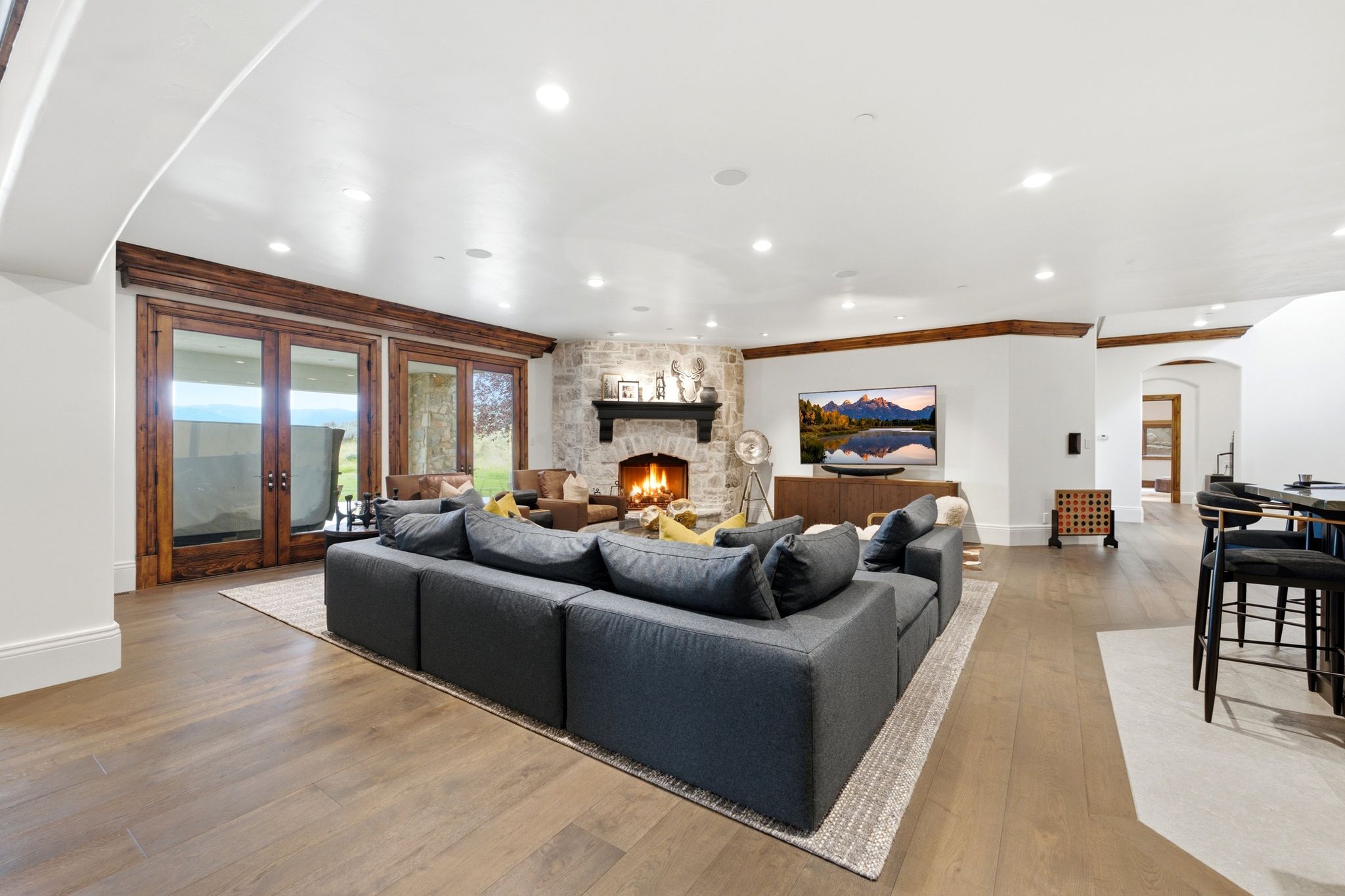 Spacious living area featuring a corner stone fireplace, wood-finish flooring, and recessed lighting