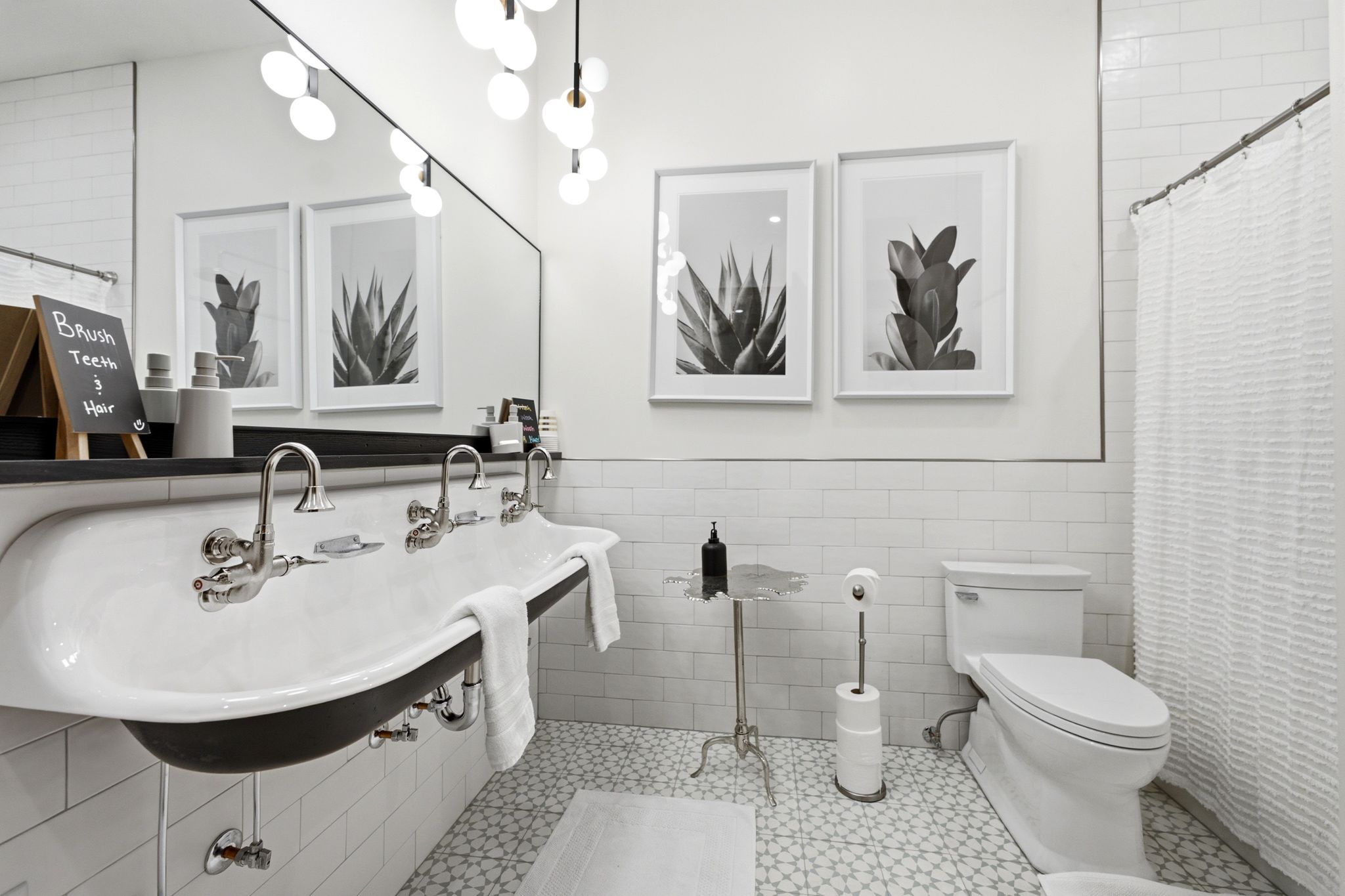 Double trough sink with wall-mounted chrome fixtures, white subway tile walls, geometric pattern floor tile, and a modern globe light fixture