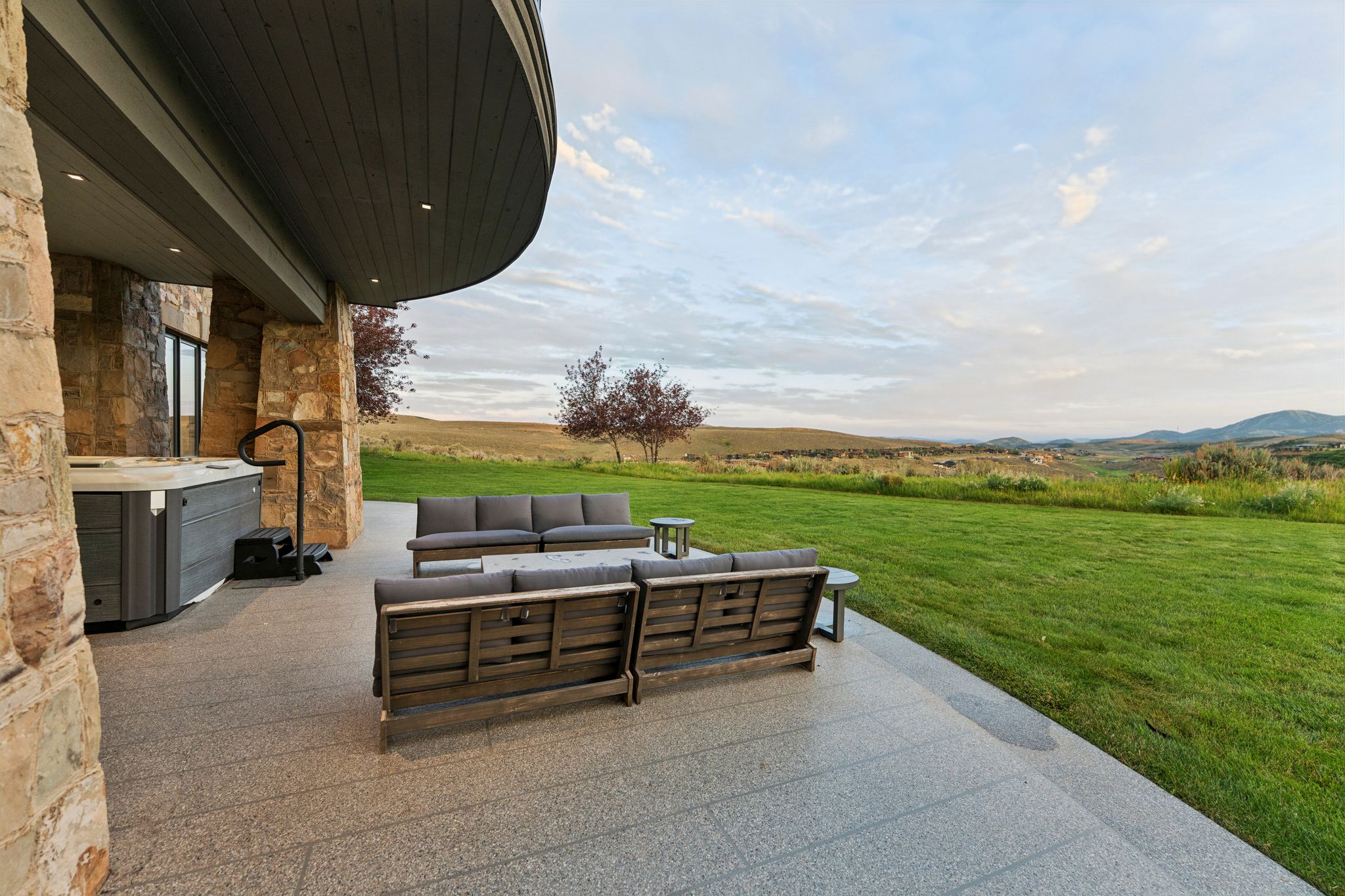 Expansive outdoor patio featuring a built-in hot tub, durable stone flooring, and a curved, covered ceiling with recessed lighting