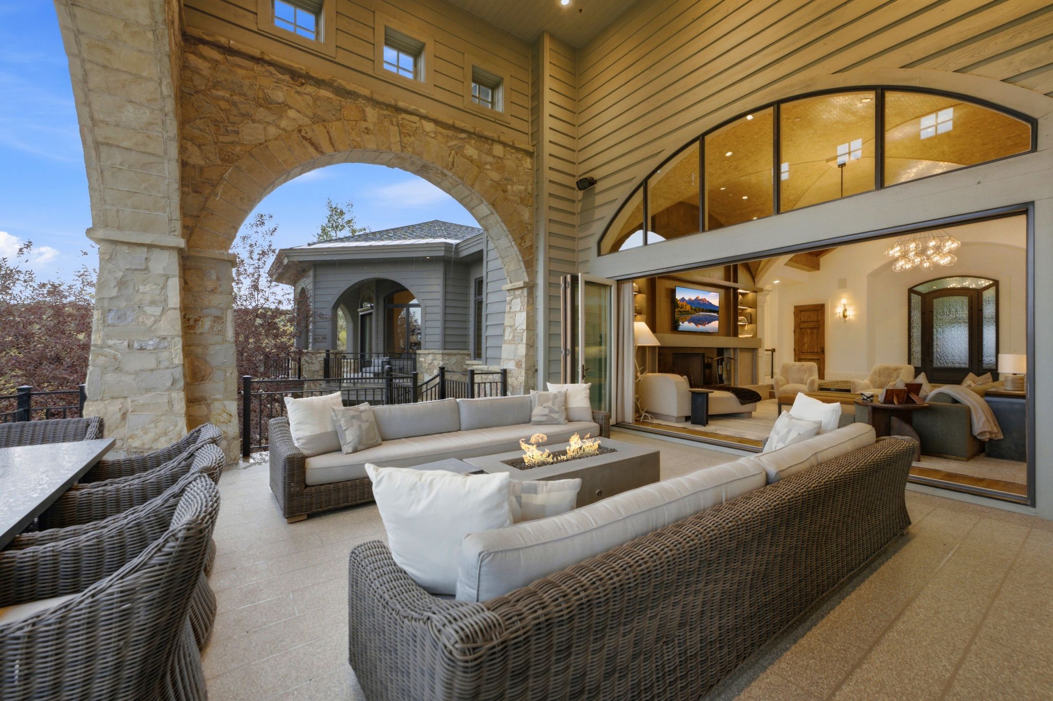 Expansive outdoor patio with stone arches and a fire pit, featuring a large dining area and direct access to the interior via sliding glass doors