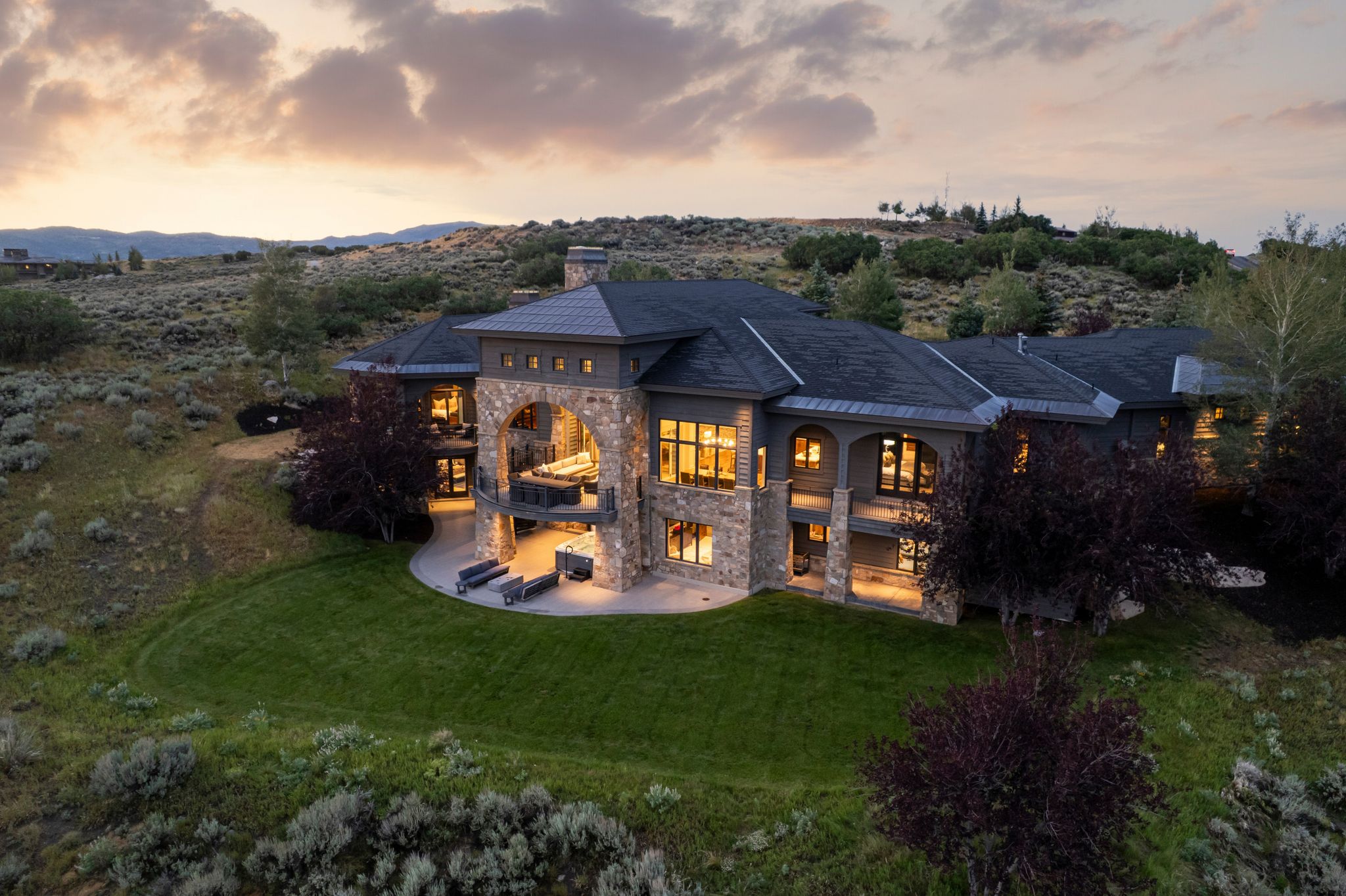 Expansive estate featuring stone and stucco siding, multiple balconies, a covered patio, a manicured lawn, and mature landscaping